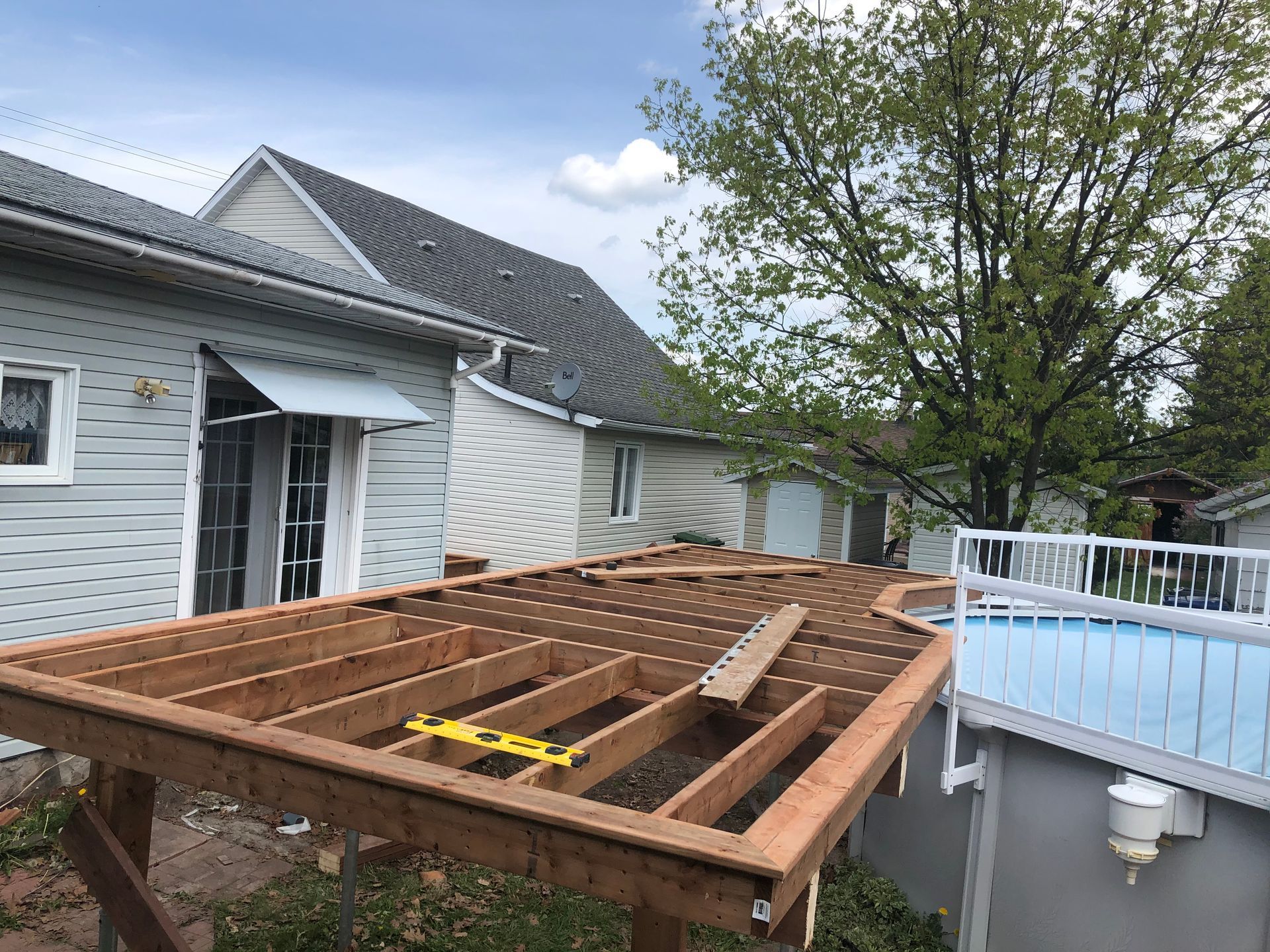Terrasse en bois en construction à côté d'une maison et d'une piscine.