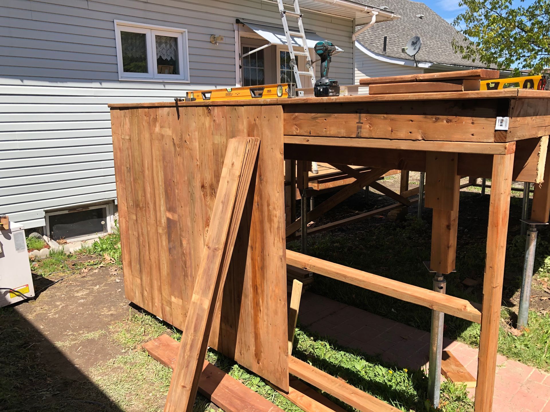 Une structure en bois en construction dans une cour. Des outils et des planches de bois sont visibles.