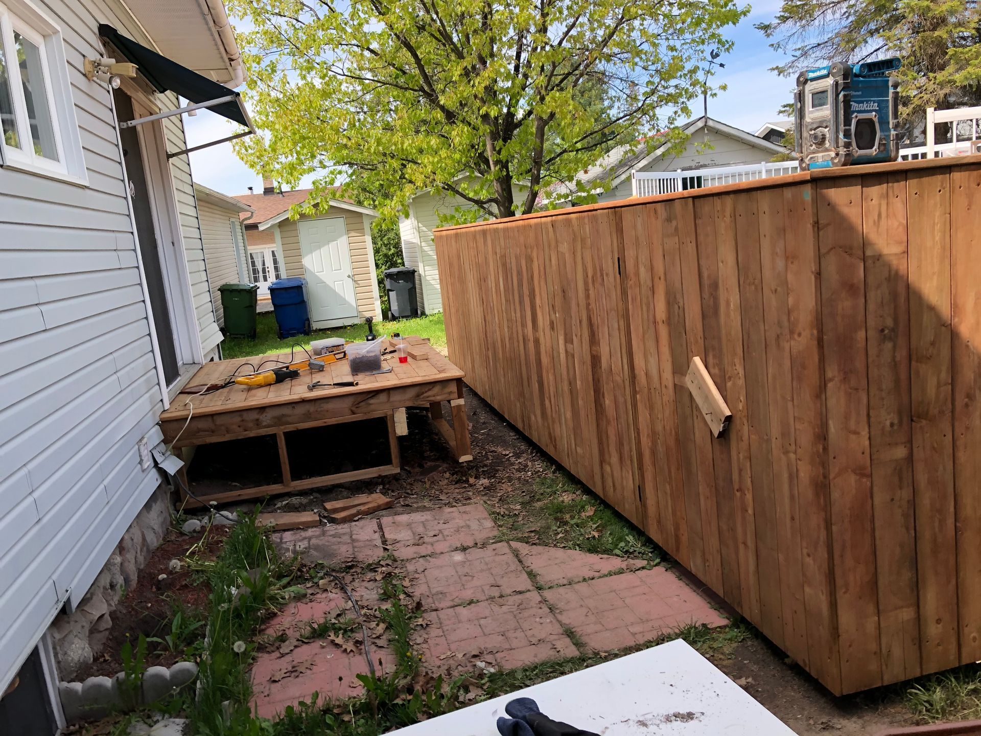 Clôture en bois et terrasse en construction à côté d'une maison avec un revêtement blanc et un patio.