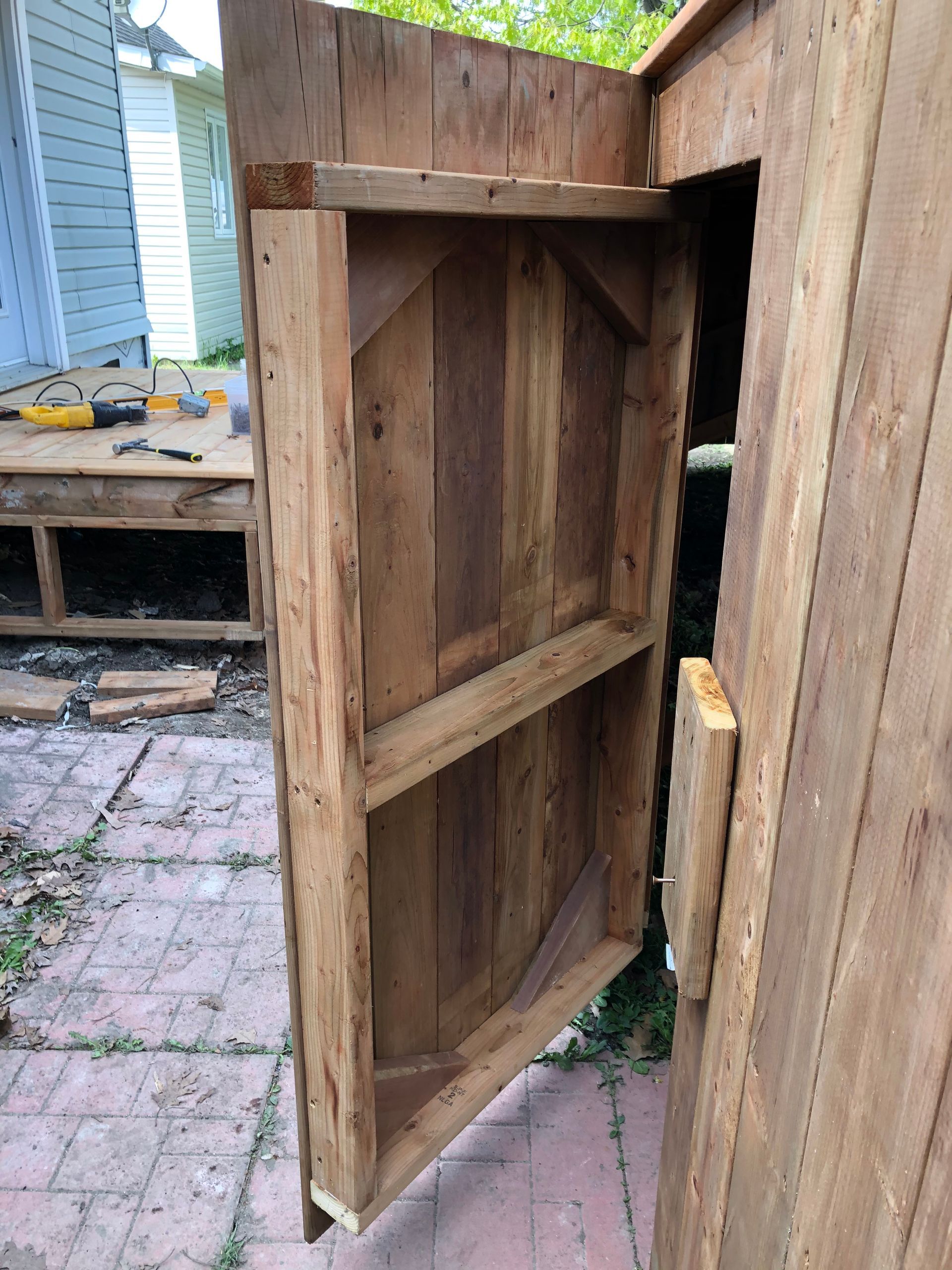 Porte d'abri en bois entrouverte, laissant entrevoir l'intérieur. À l'extérieur, porte en bois de récupération.