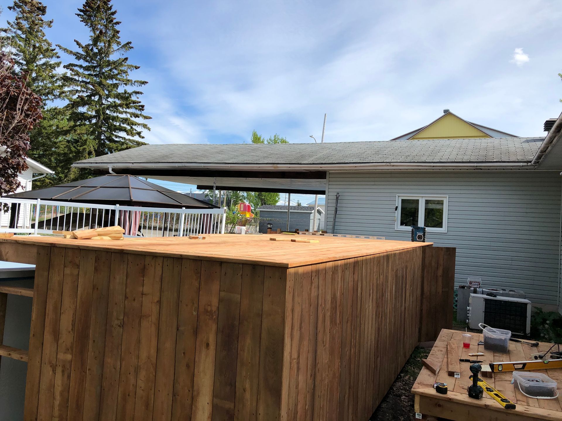 Construction d'une clôture en bois dans un jardin jouxtant une maison au bardage bleu. Journée ensoleillée.