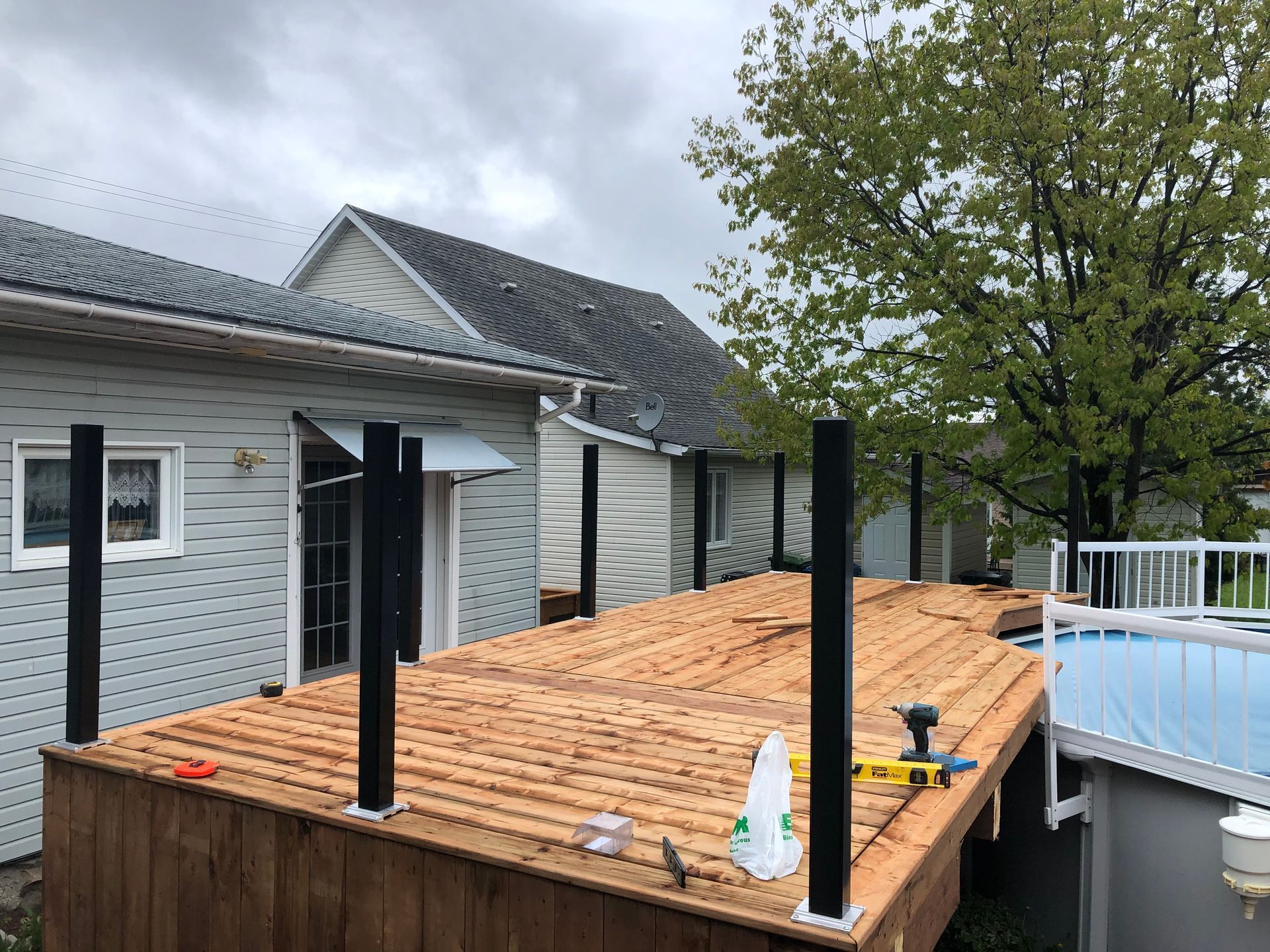Construction d'une terrasse : terrasse en bois avec poteaux noirs près d'une maison et d'une piscine hors sol. Ciel nuageux.