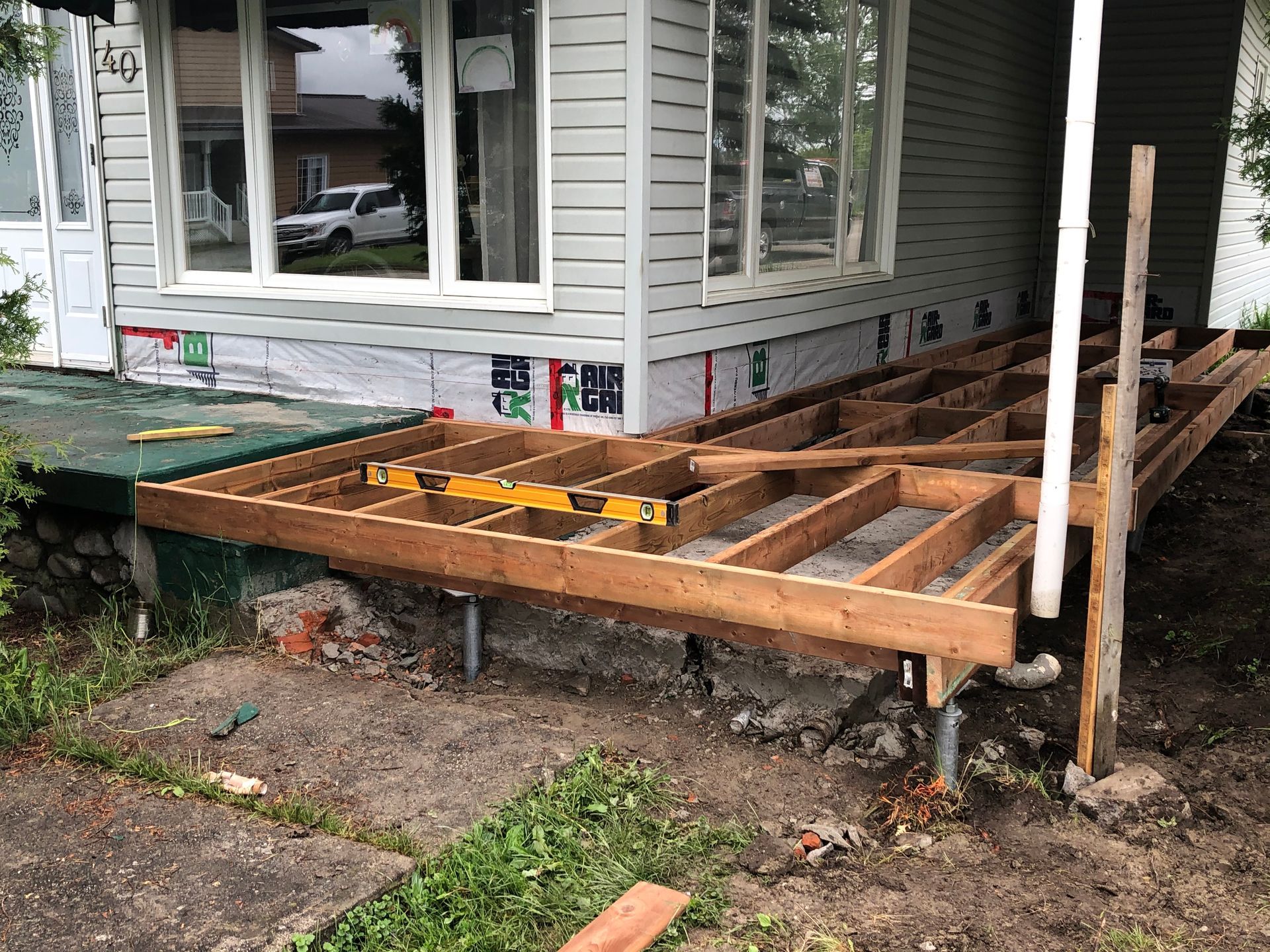 Terrasse en bois en construction sur un porche, la maison étant en arrière-plan.