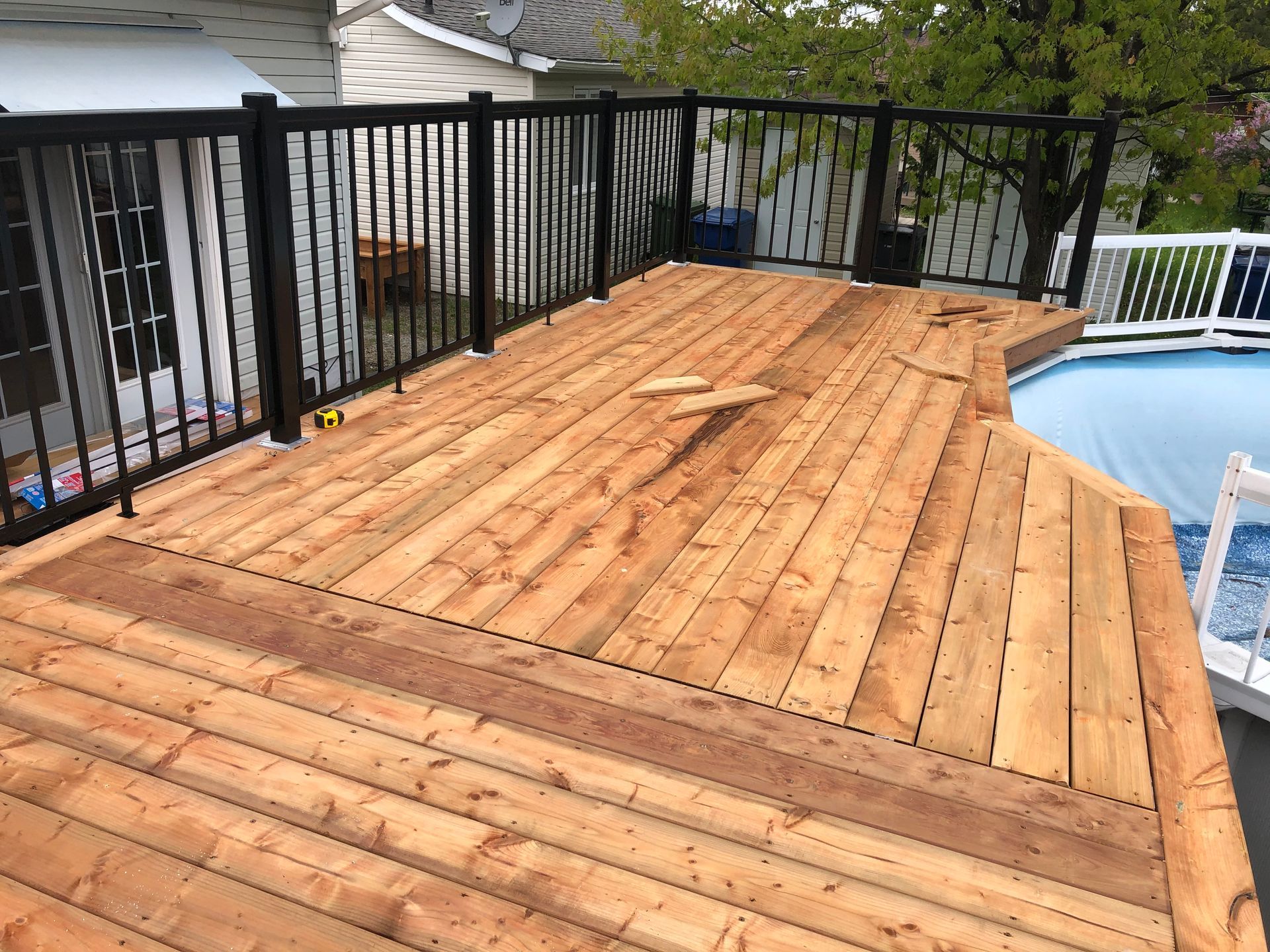 Terrasse en bois avec rambardes noires à côté d'une piscine.