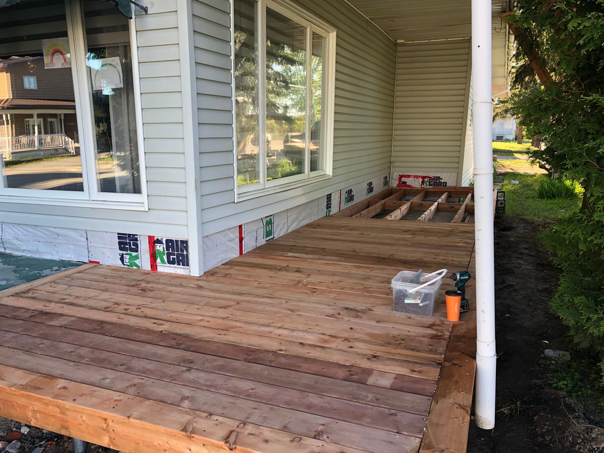 Terrasse en construction ; planches de bois partiellement installées sur la façade d'une maison.