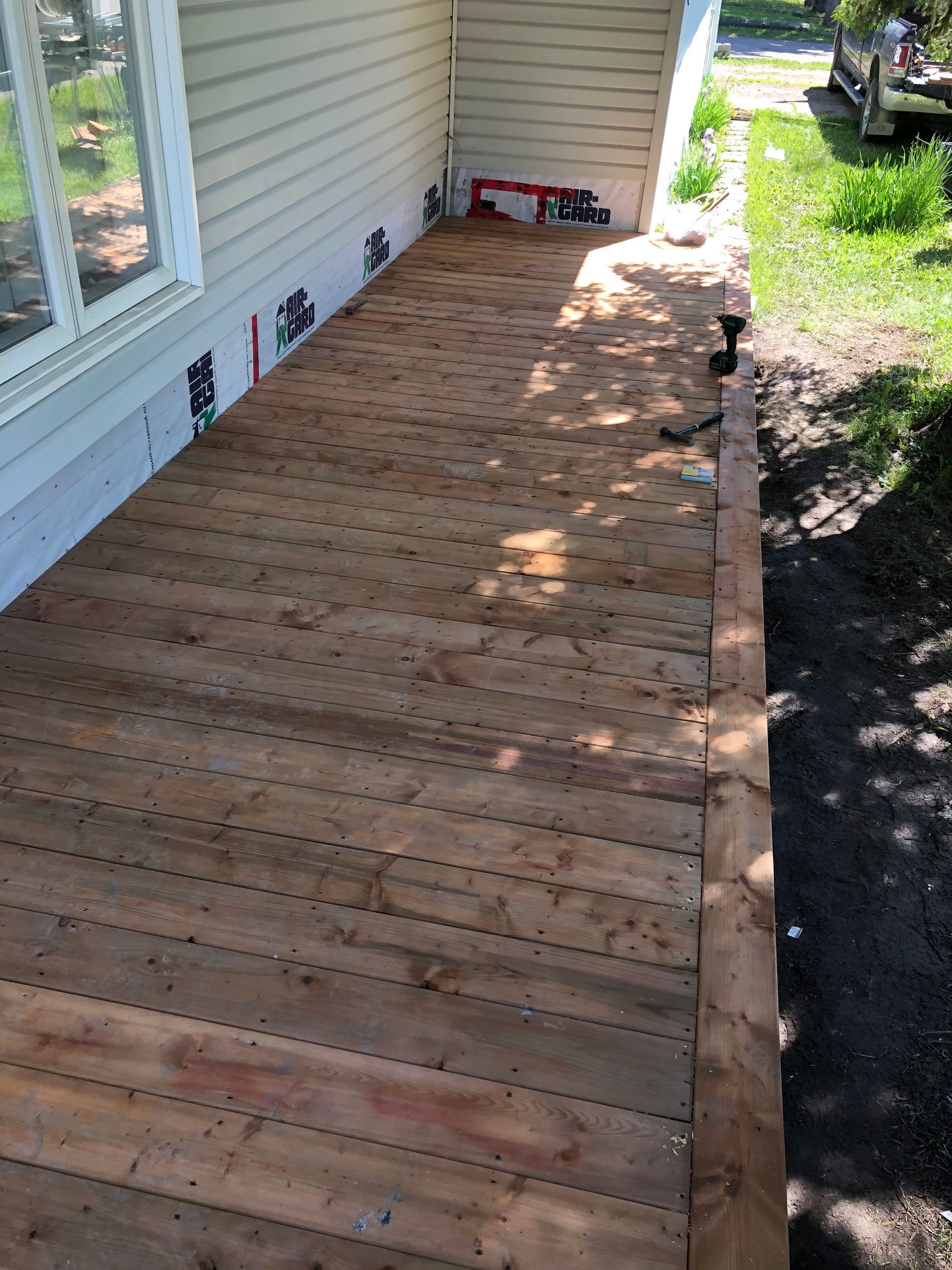Terrasse en bois longeant une maison claire. Les planches sont usées par le temps et présentent de nombreux trous de vis. 
