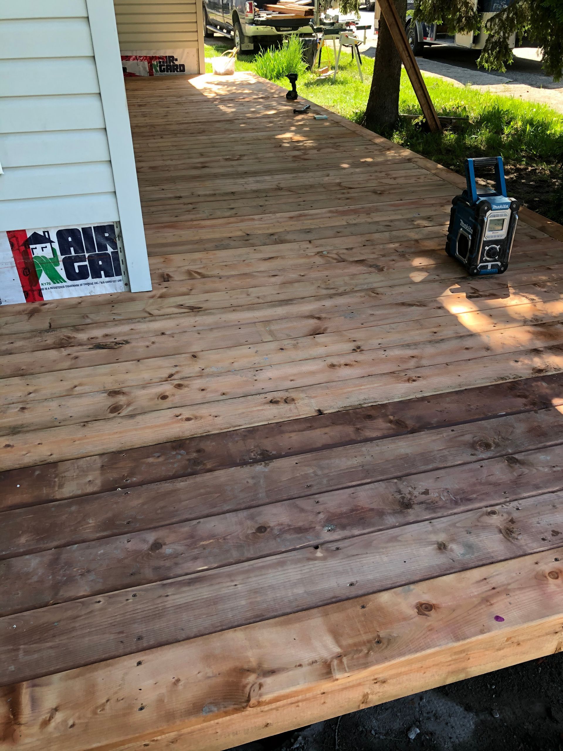Terrasse en bois jouxtant une maison blanche où se trouve un outil électrique. La lumière du soleil brille sur le bois.