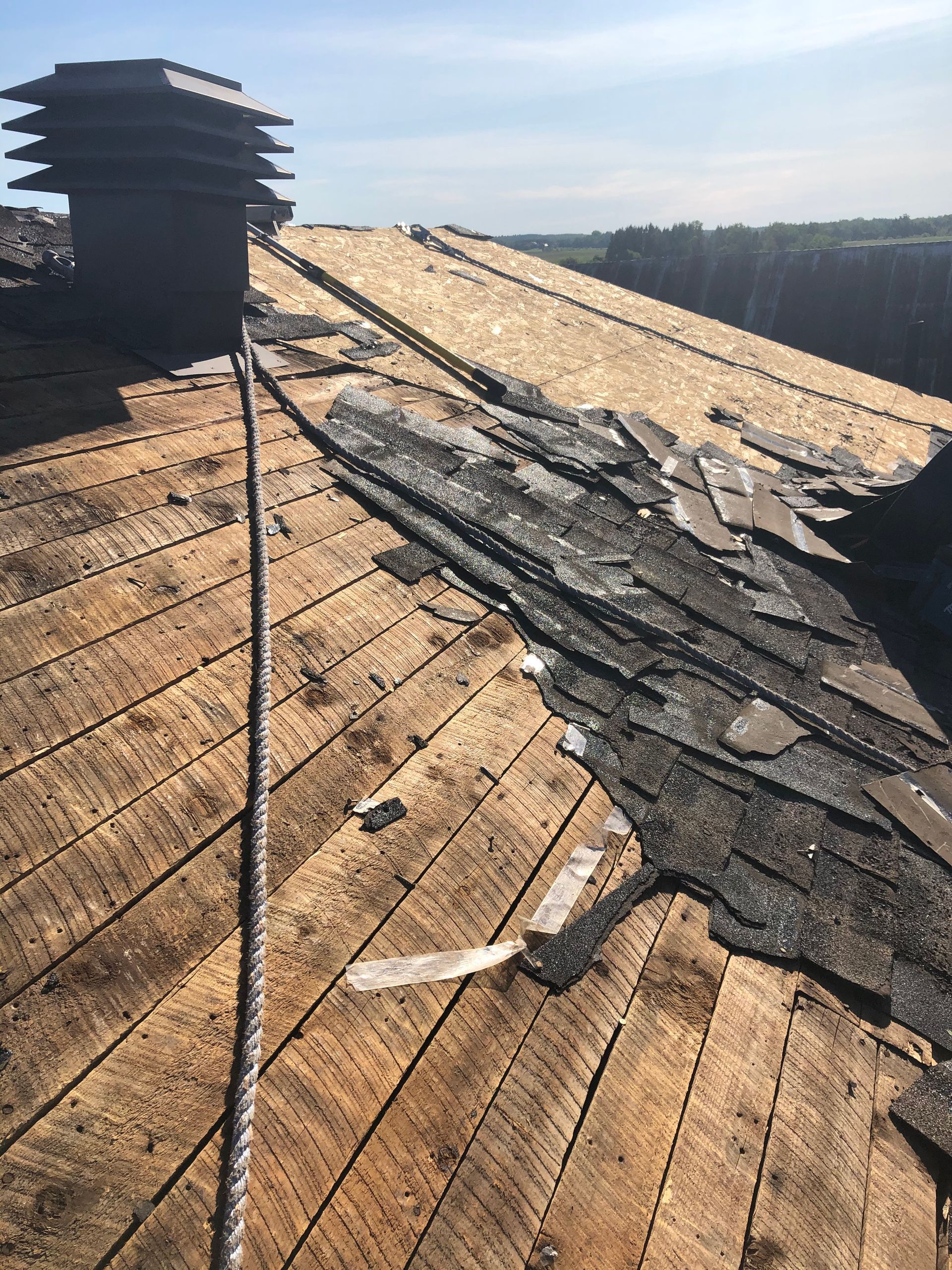 Toiture en bardeaux d'asphalte endommagée, partiellement décapée, révélant une sous-couche en bois près de la cheminée.