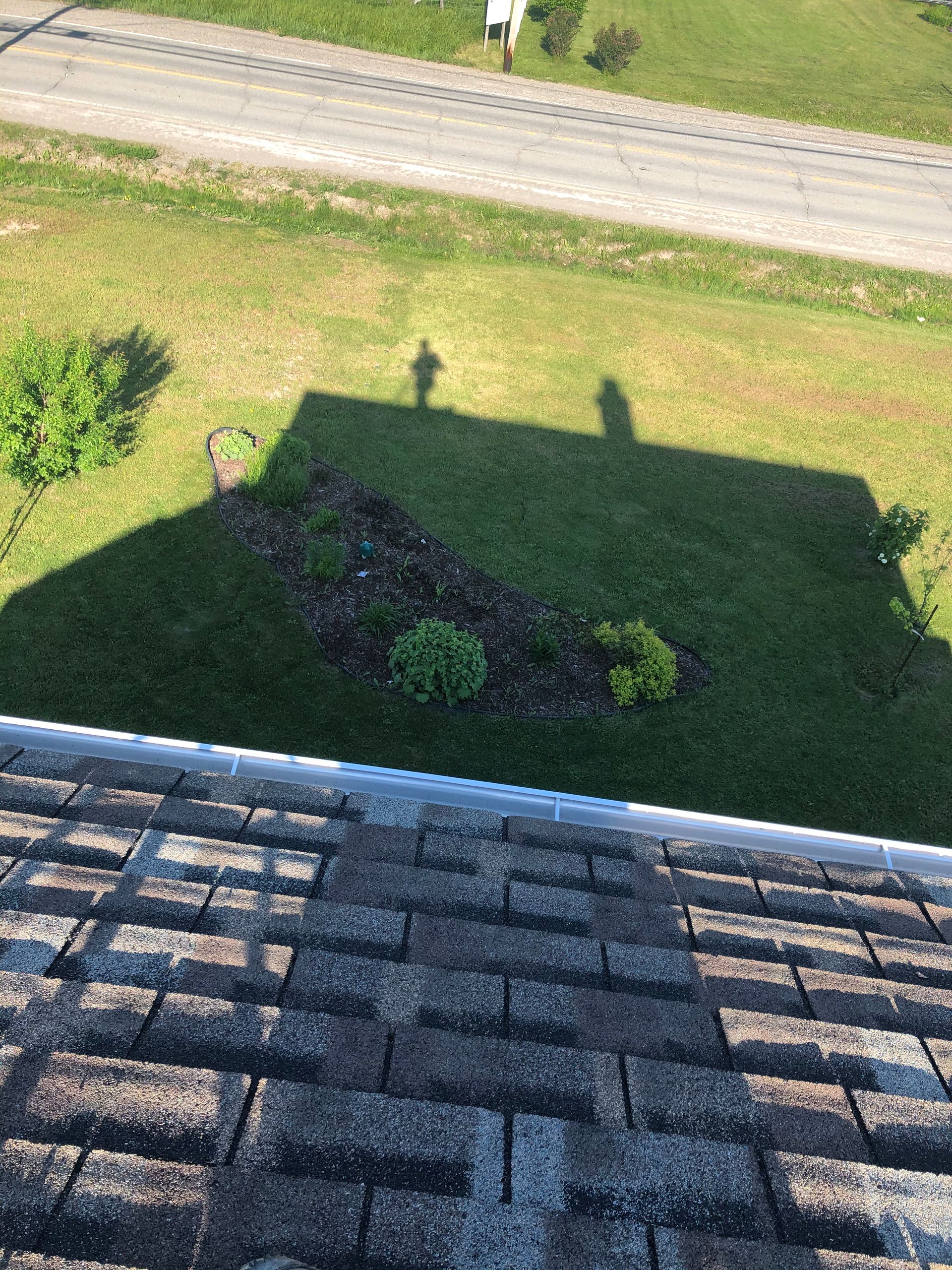 Ombre d'une personne sur l'herbe, toit au premier plan, rue à l'arrière-plan.