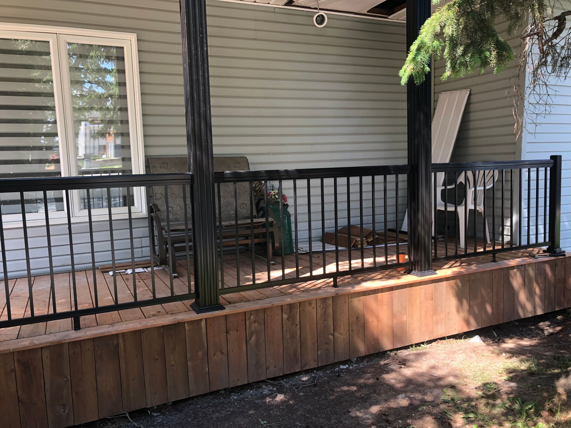 Rambarde noire sur une terrasse en bois avec une maison vert clair en arrière-plan.