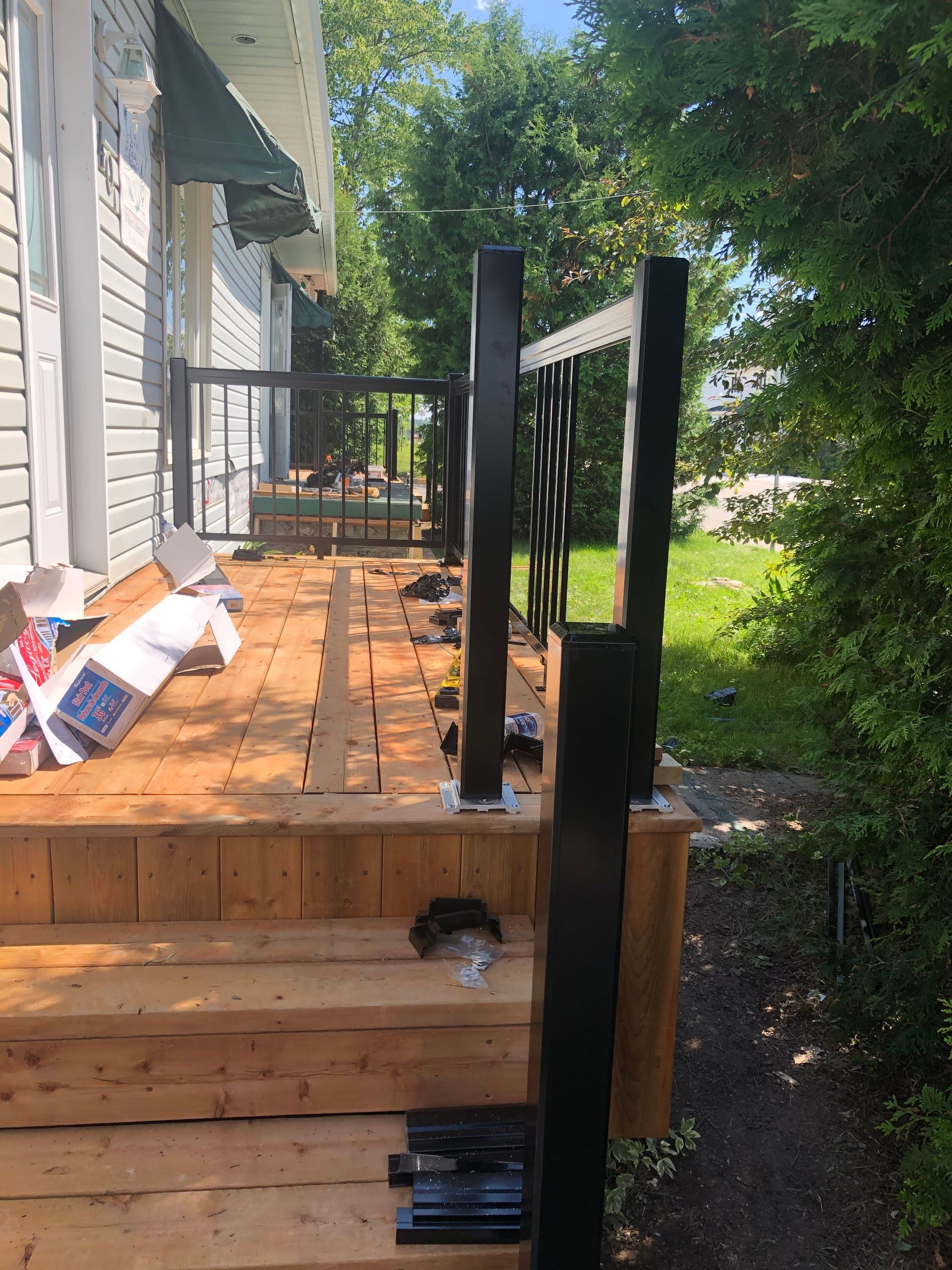 Une terrasse en bois avec une rambarde en métal noir est installée à l'extérieur d'une maison.