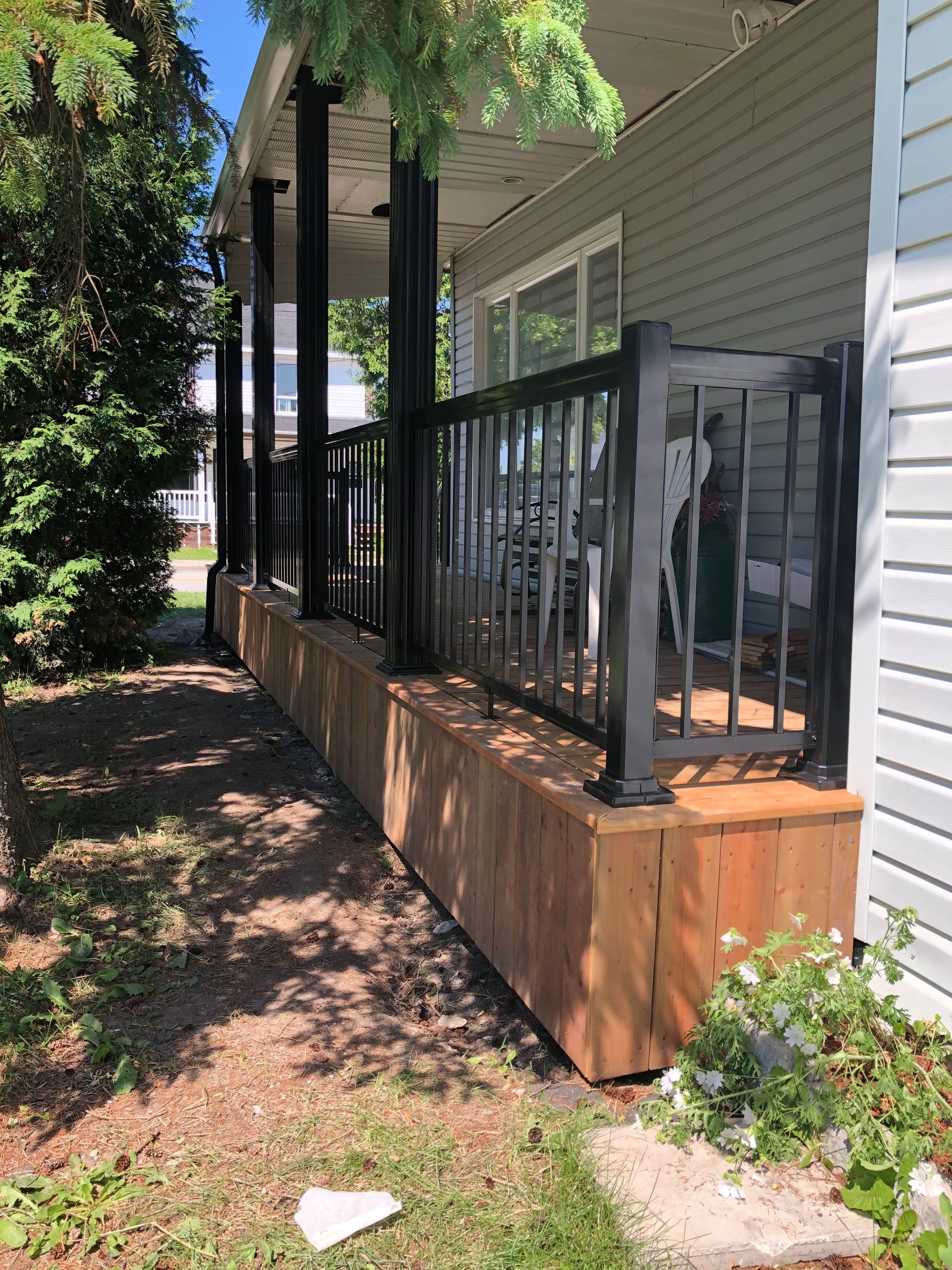 Maison avec terrasse en bois et balustrade noire. Vue extérieure, journée ensoleillée.