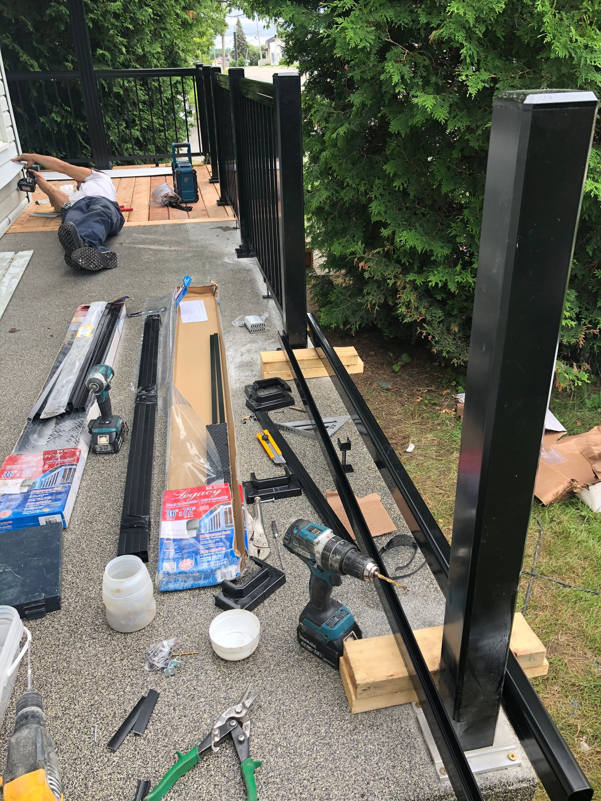 Un homme installe une rambarde en métal noir sur une terrasse, des outils et des matériaux sont éparpillés autour.