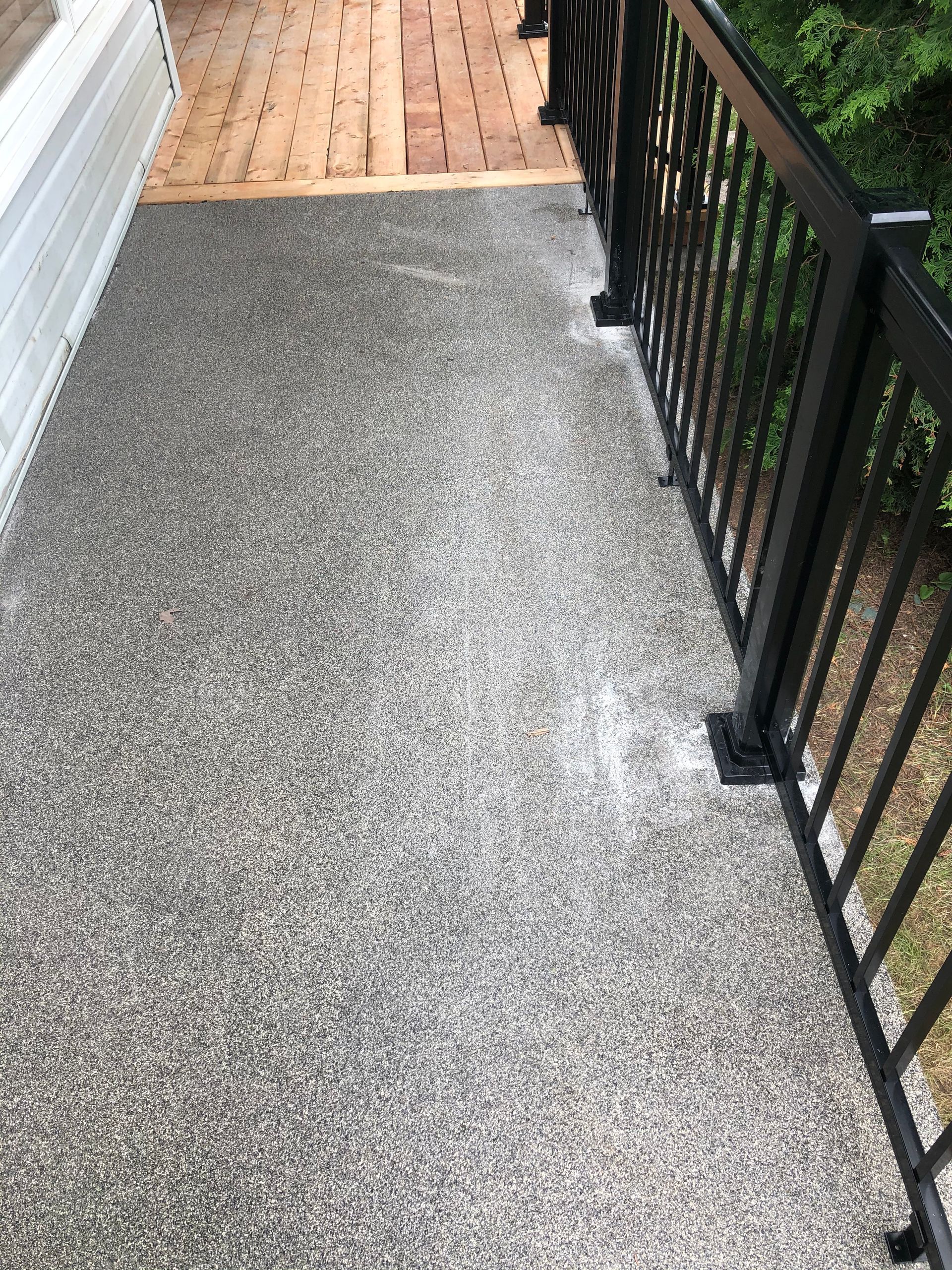 Un sol de terrasse gris moucheté avec une rambarde noire mène à une terrasse en bois.