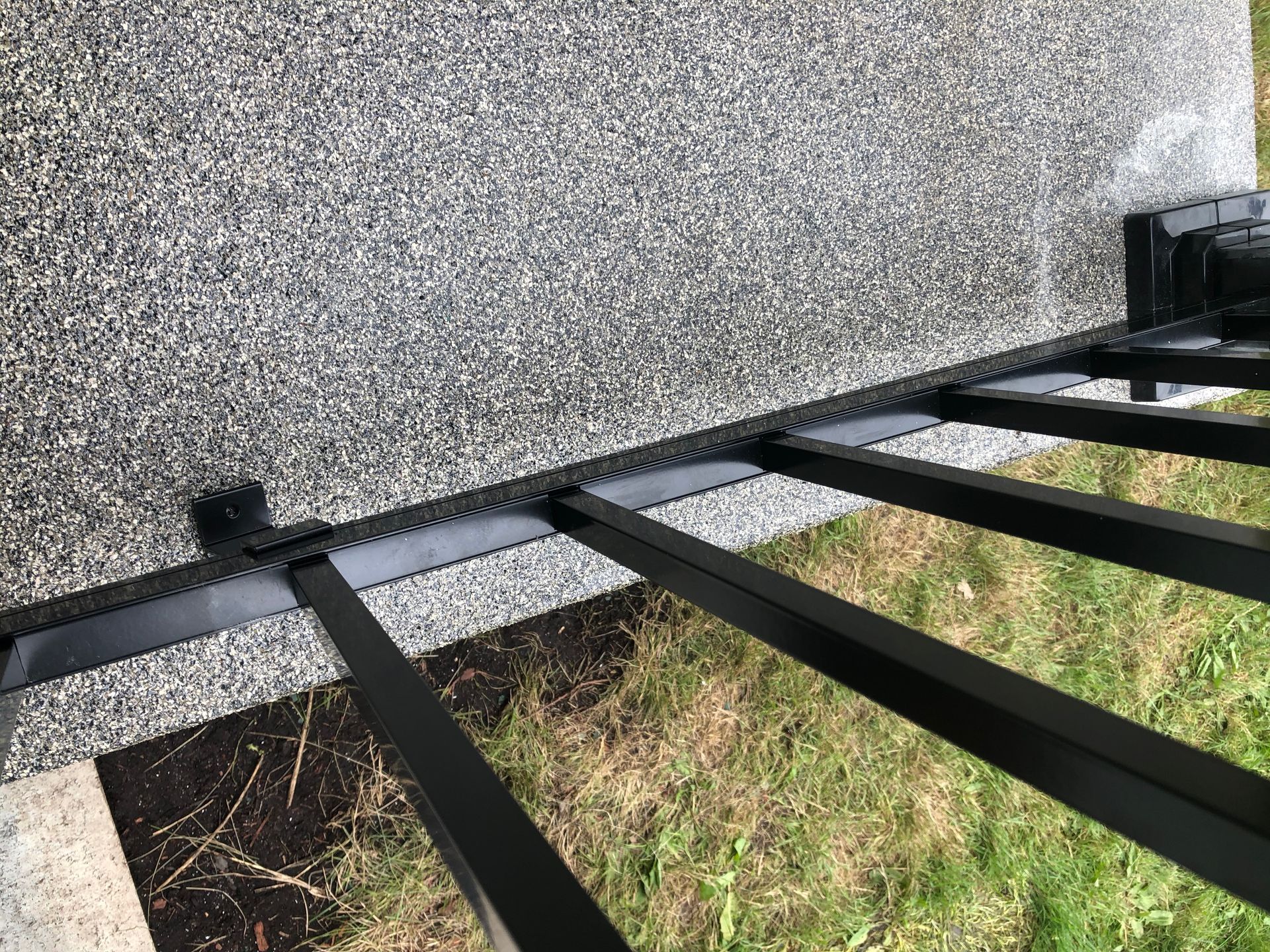 Rambarde en métal noir sur une surface gravillonnée bordée de pelouse.