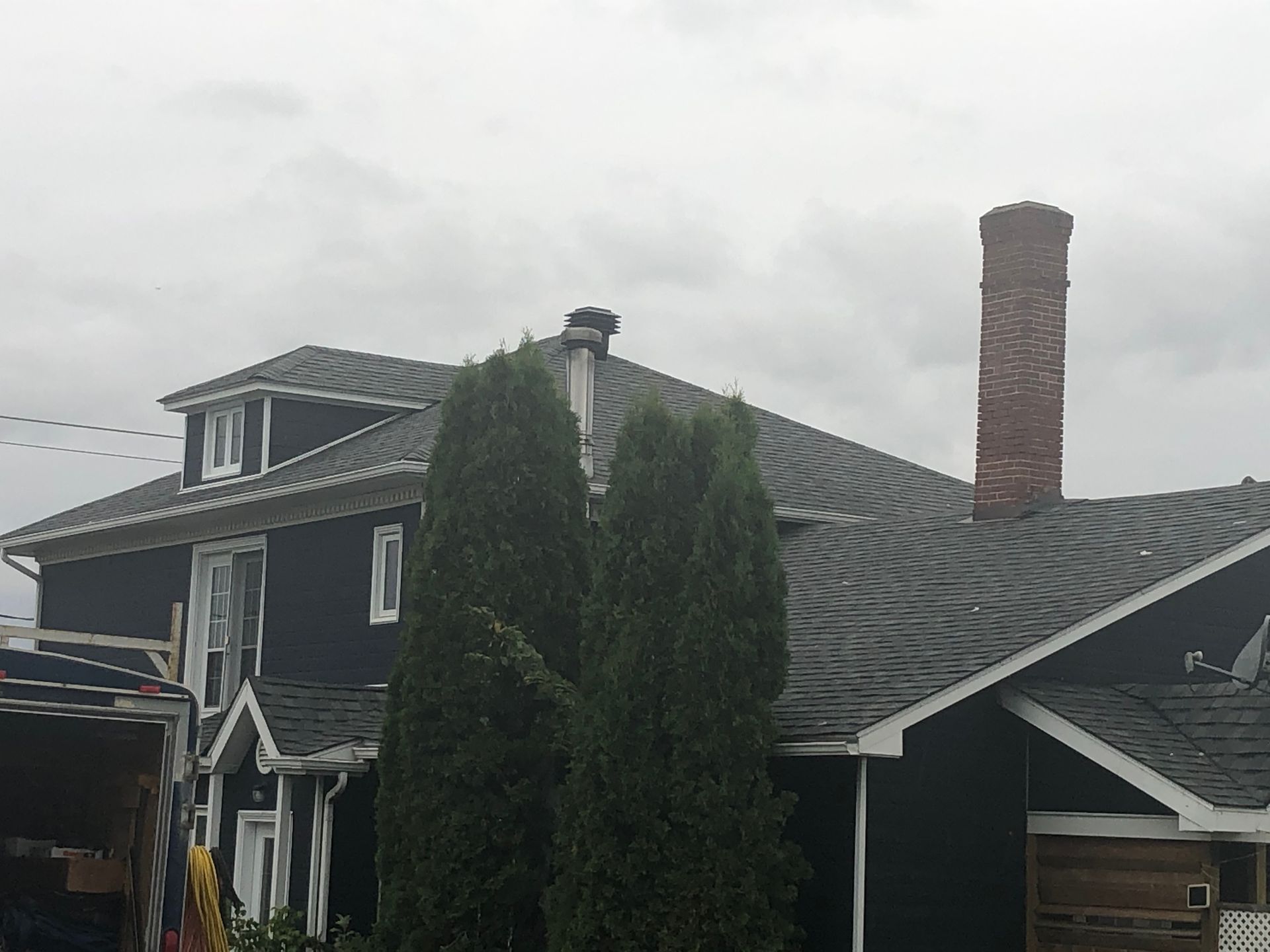 Maison sombre au toit gris et à la cheminée en briques, sous un ciel nuageux.