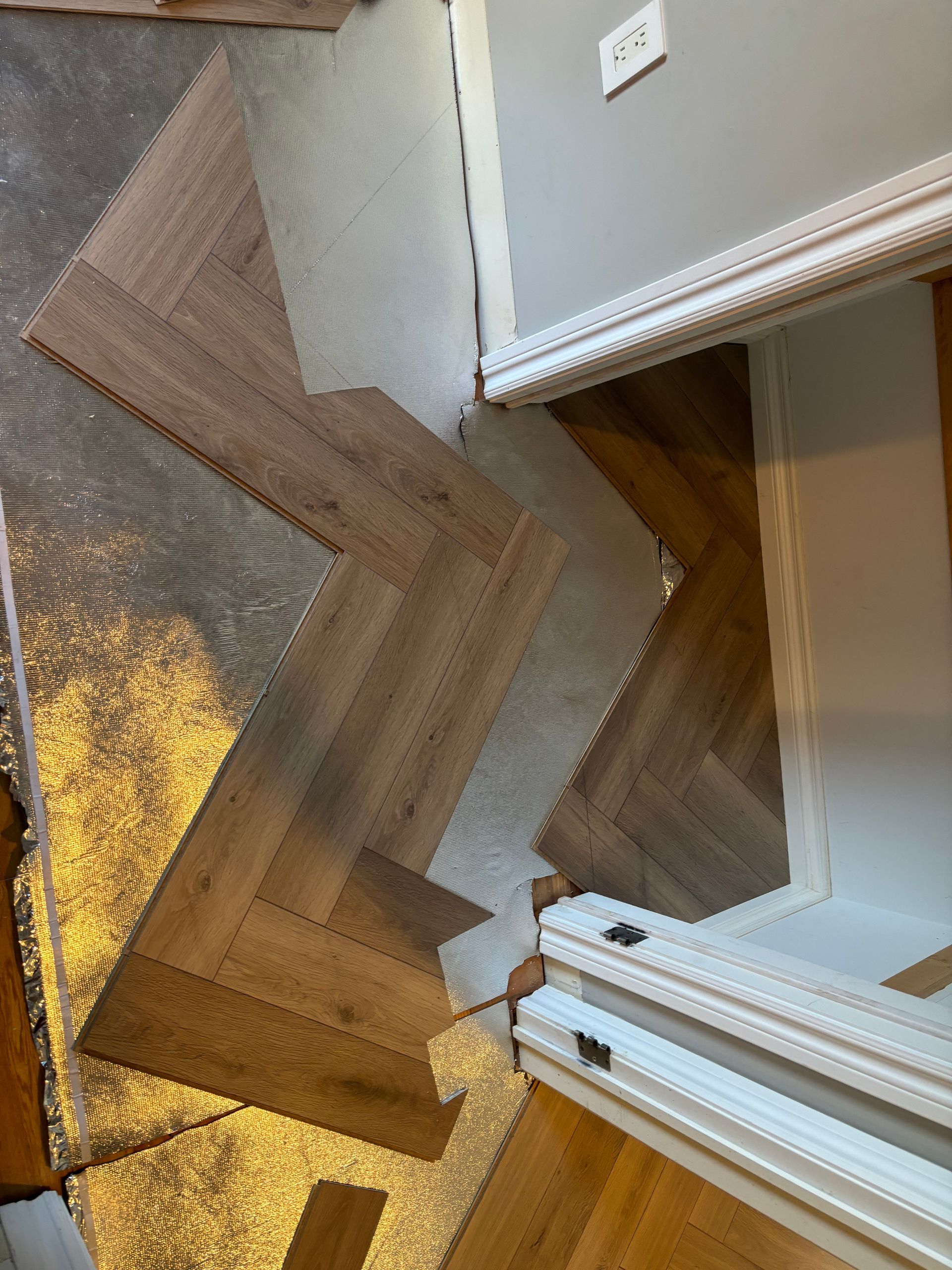 Pose d'un parquet à chevrons en cours, la couche isolante est visible.