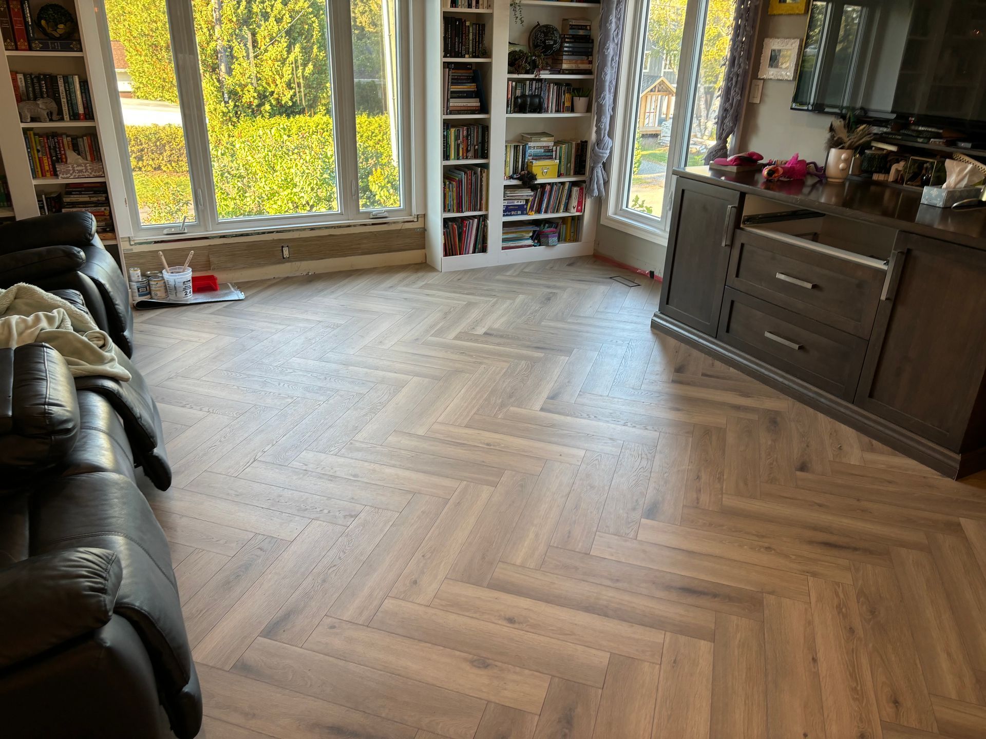 Parquet à chevrons dans un salon avec bibliothèque, meuble sombre et grandes fenêtres.