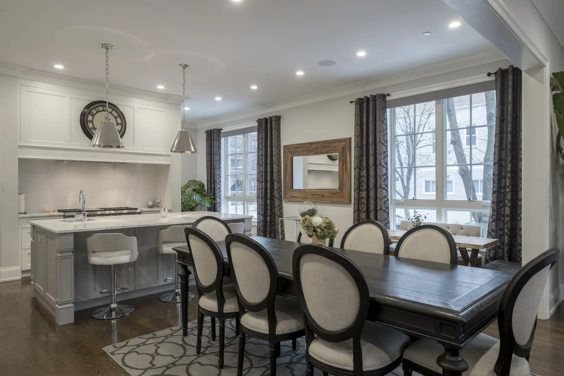 Bright modern dining room with a black table, upholstered chairs, and adjacent kitchen with white cabinets