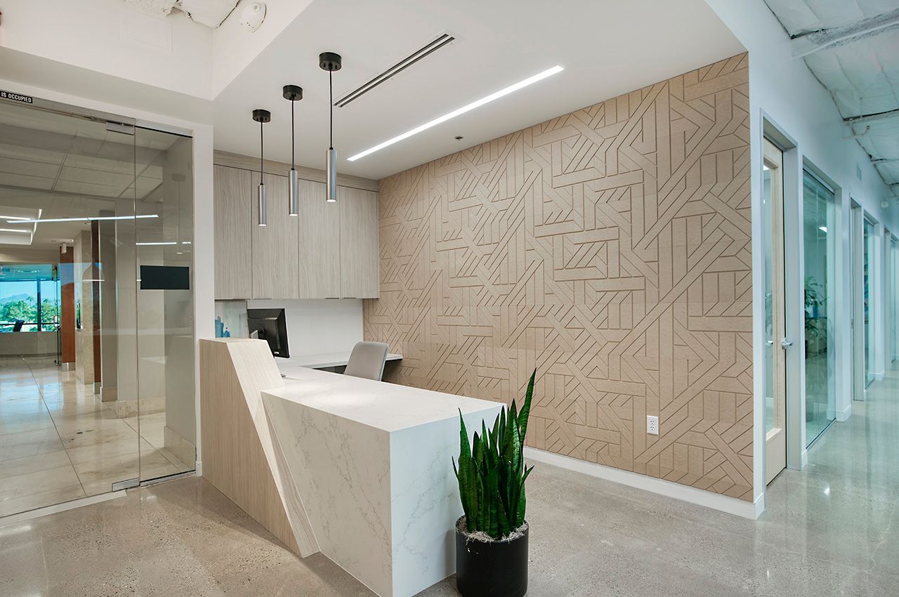 Modern office lobby with a white reception desk, textured wall, and glass hallway to the left.