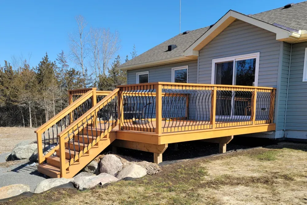 Wooden deck with stairs and black railing attached to a house on a sunny day