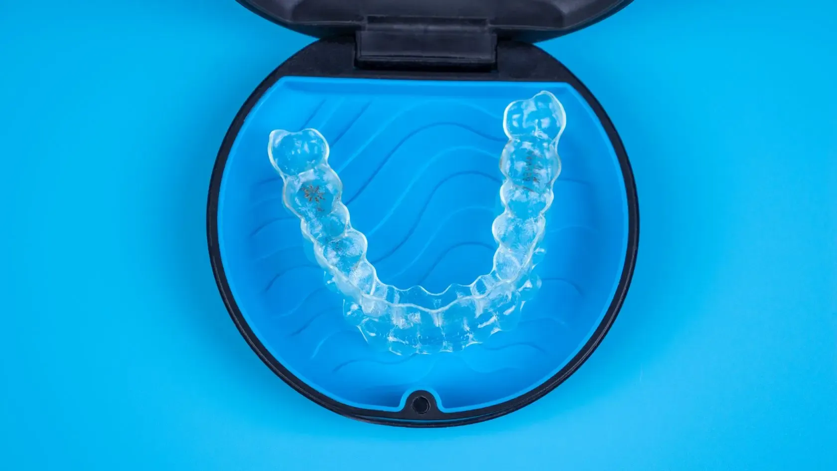 Clear aligners in an open blue case on a blue background.