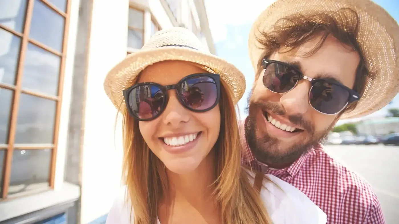 Smiling couple wearing sunglasses and straw hats outdoors, sunny day.