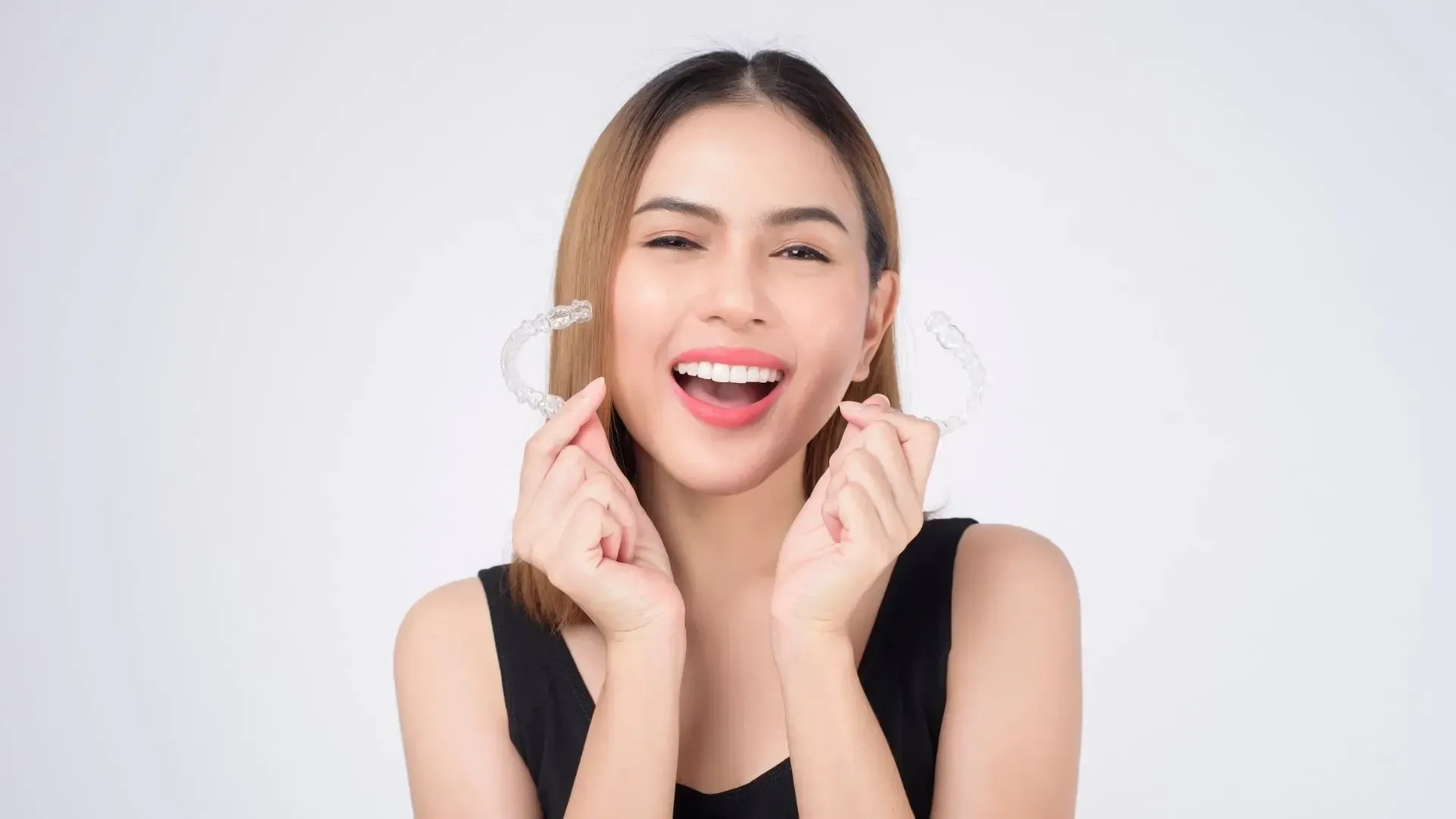 A woman is holding a clear retainer in her hands and smiling.