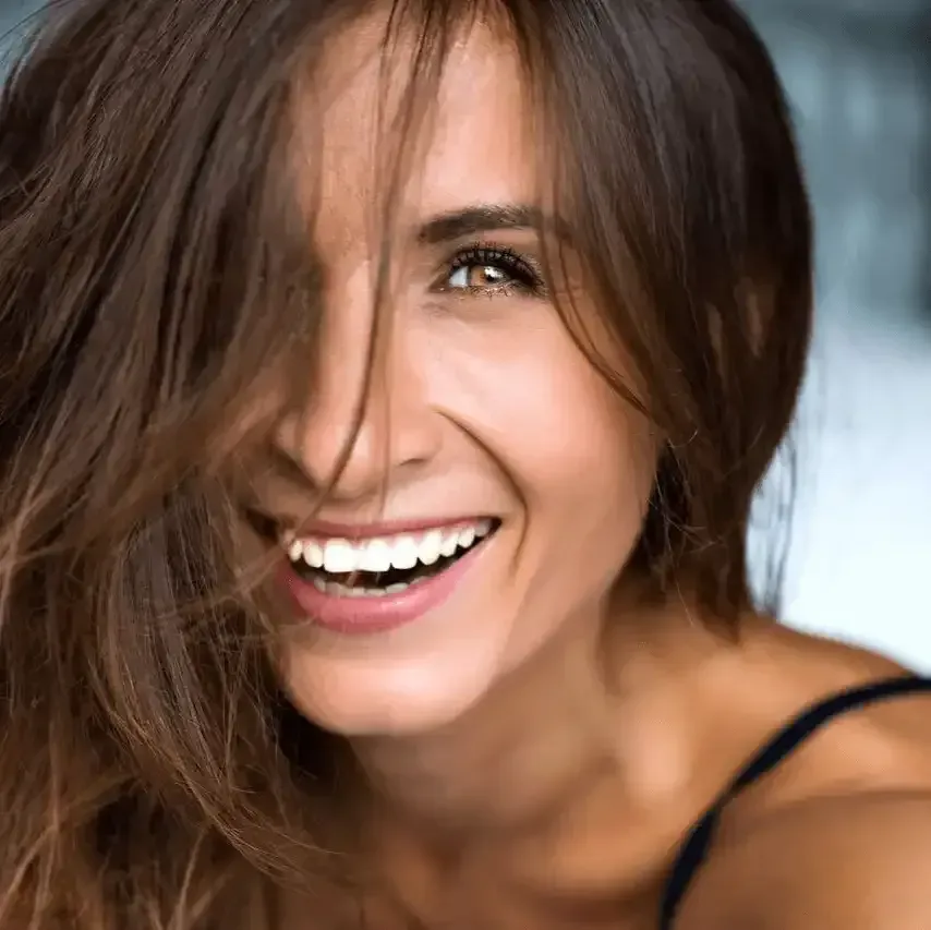 A close up of a woman smiling with her hair covering half of her face.