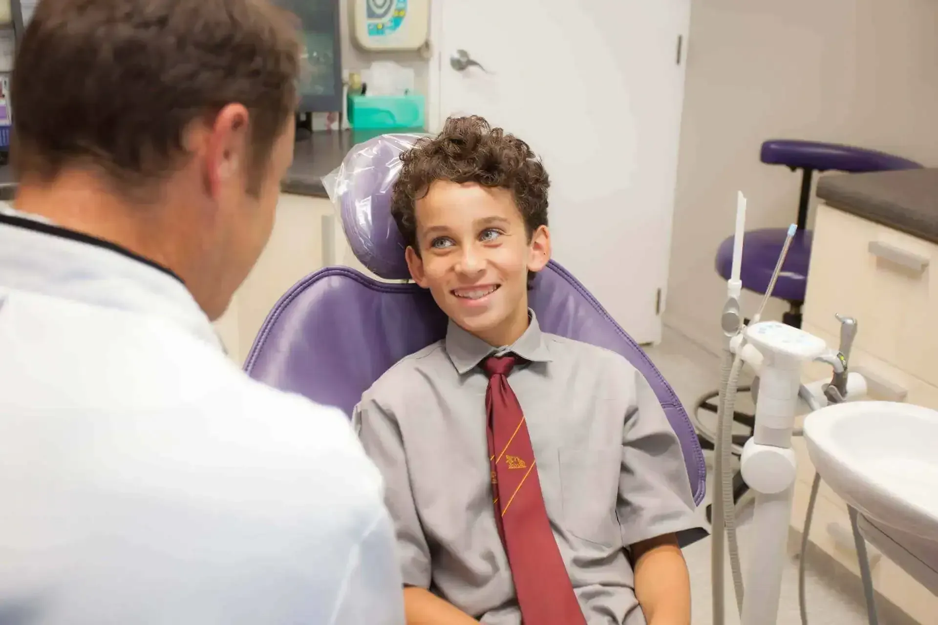 A young boy is sitting in a dental chair talking to a dentist