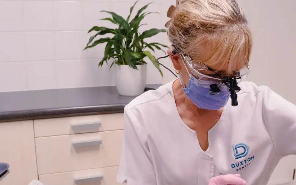 Dentist wearing mask and loupes examining a patient in an office setting.