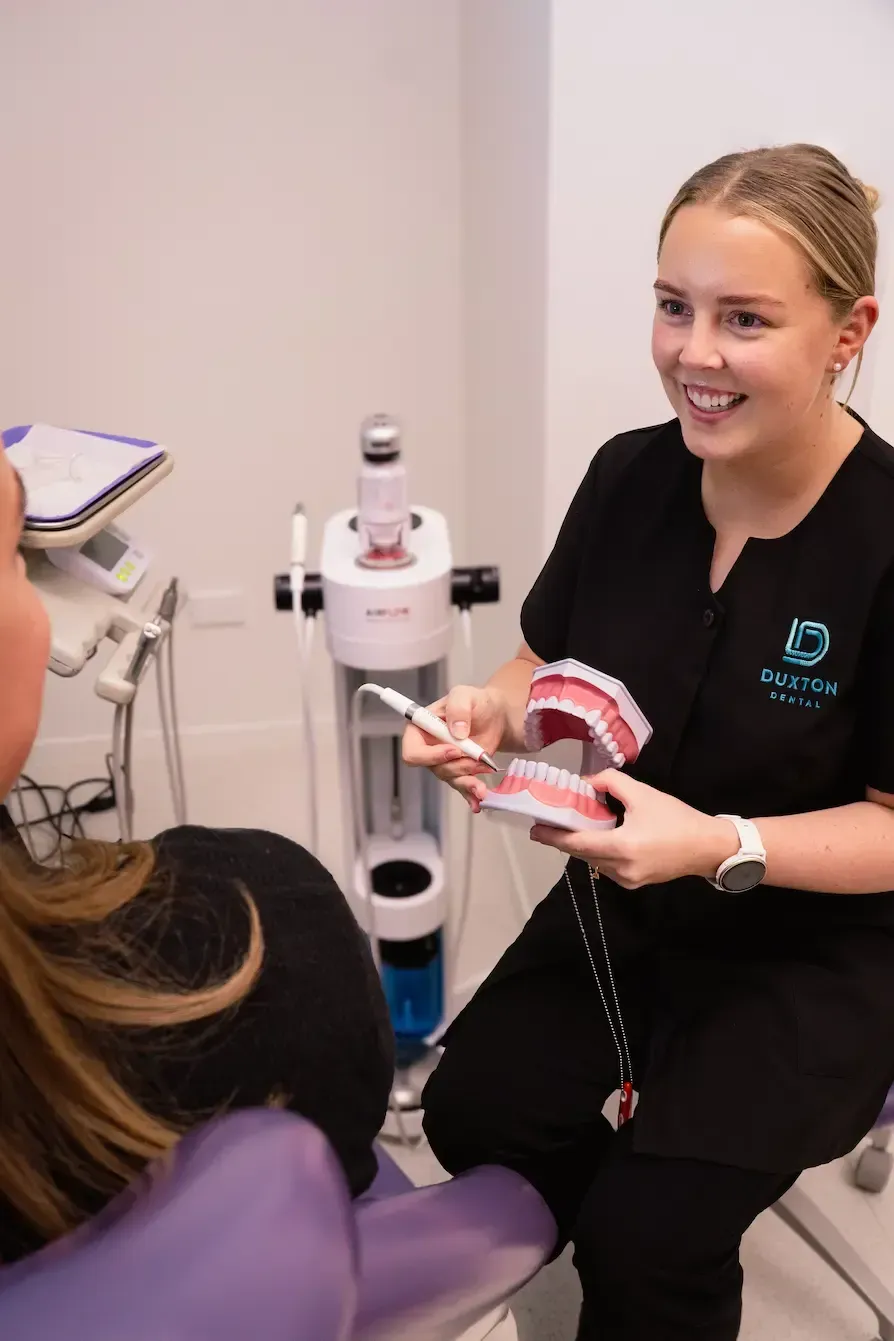 Dentist showing dental model to a smiling patient in a clinic, with treatment equipment nearby