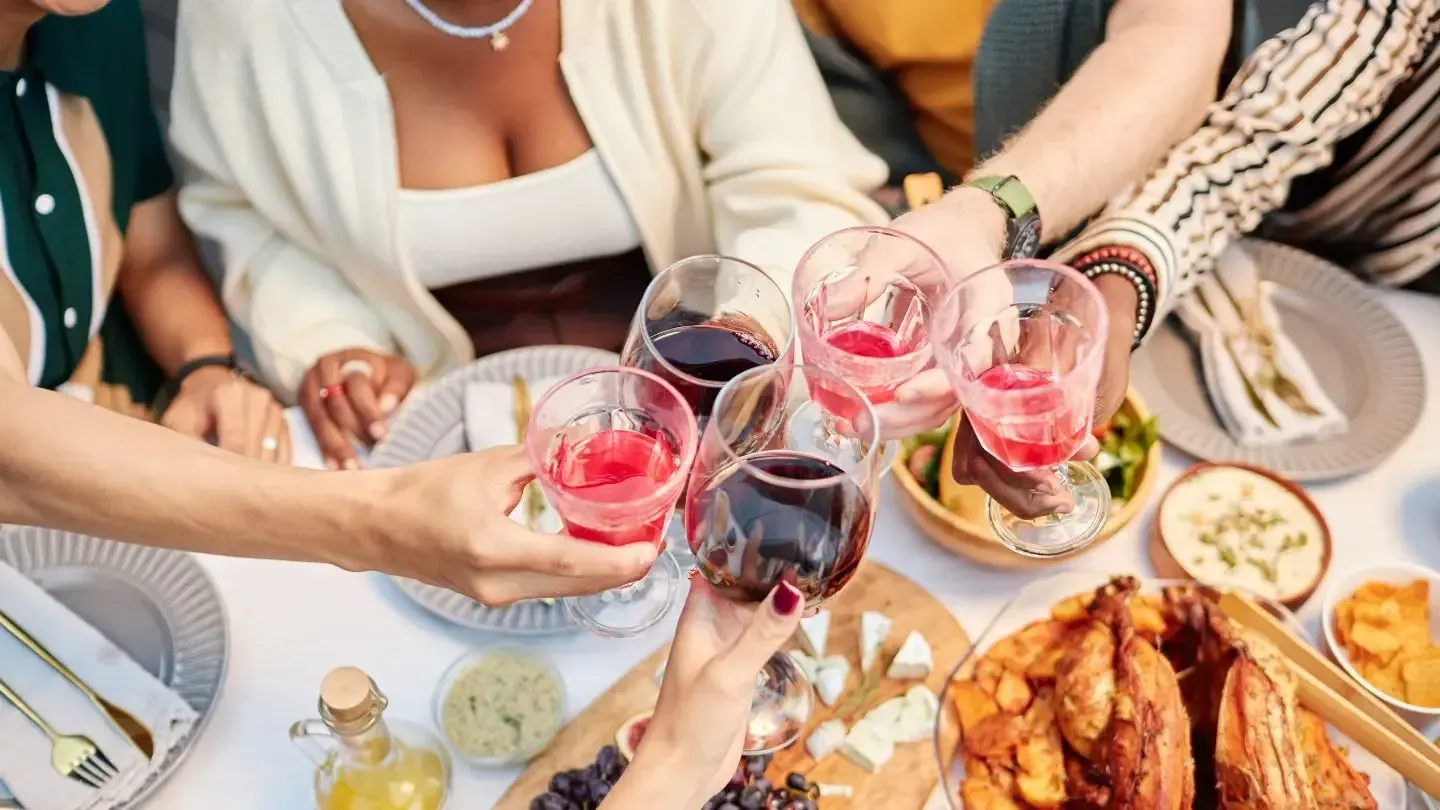 A group of diverse people making a toast with wine glasses over dinner.