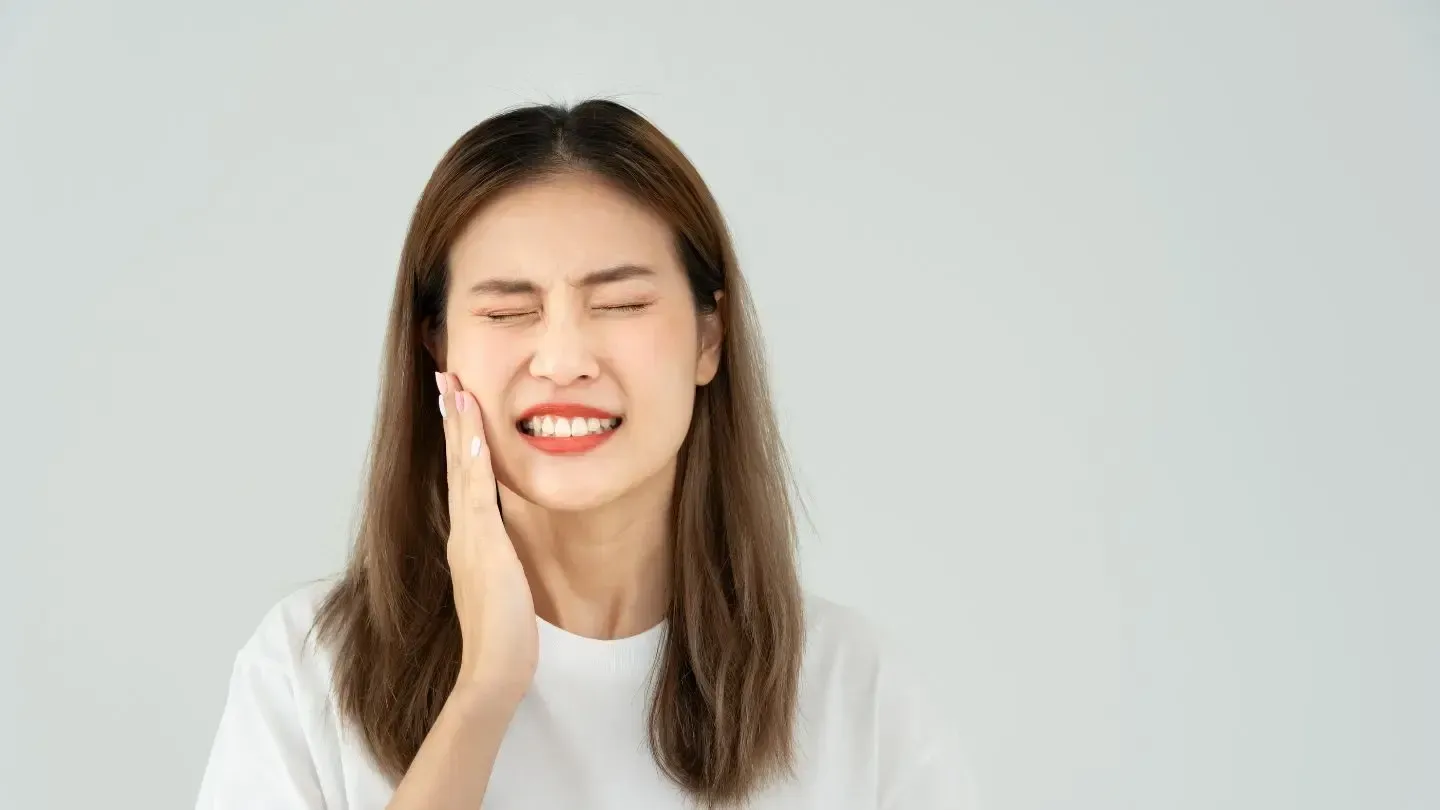 Young woman wincing, pressing hand to cheek, indicating toothache.