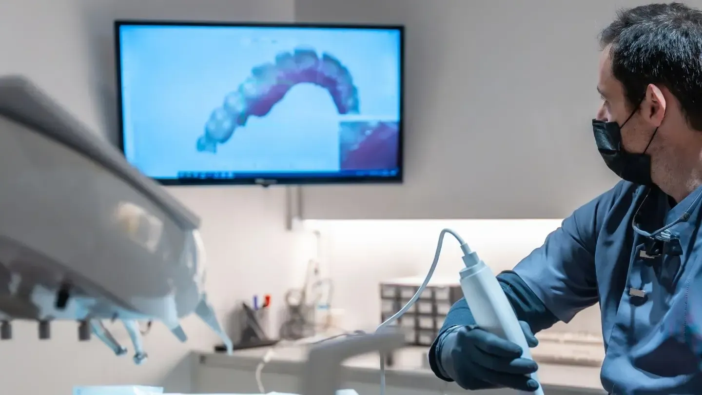 Dentist holding a scanning device, viewing teeth scan on a monitor in an office.