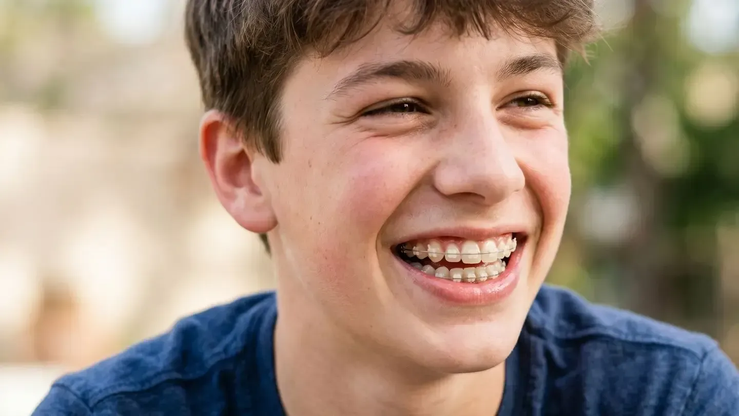 Smiling person with braces in a blue shirt, outdoors with a blurred background