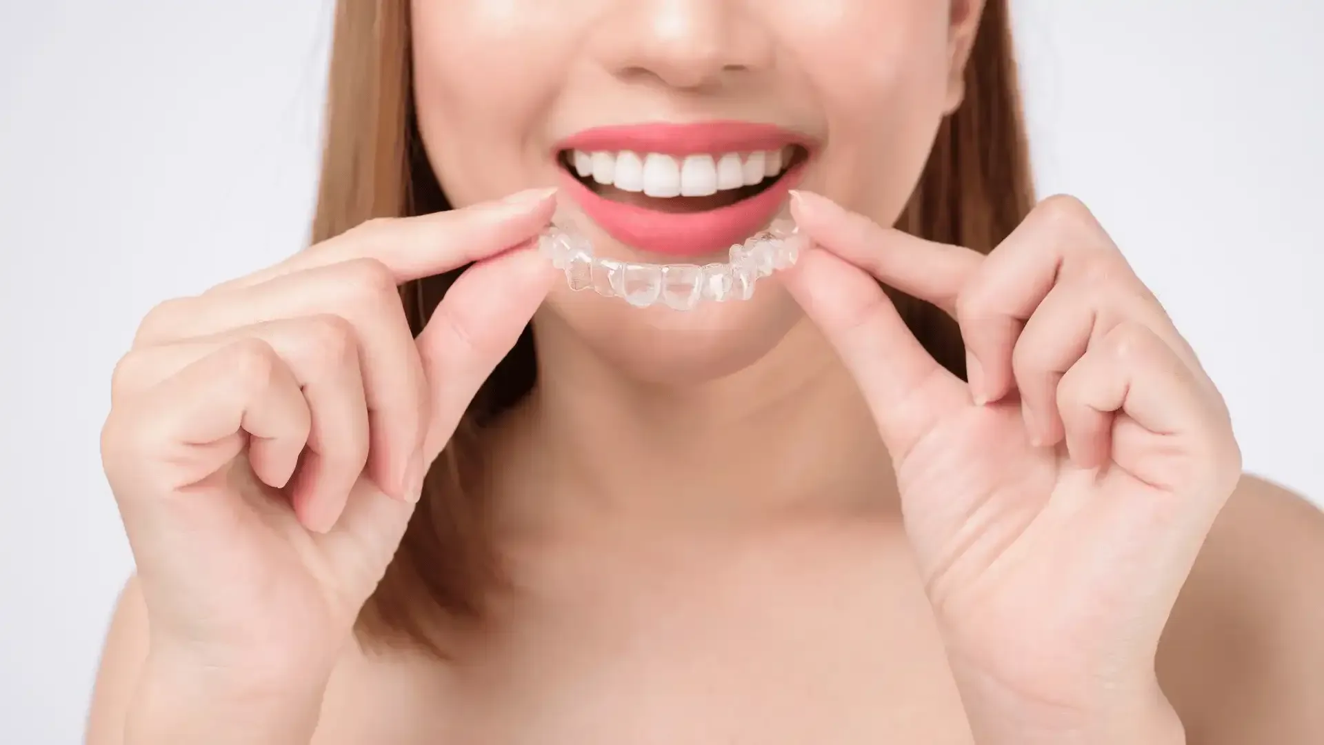 A woman is holding a clear brace in her mouth.