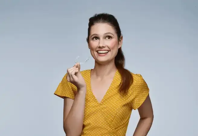 a woman in a yellow dress is smiling and holding a clear toothbrush .