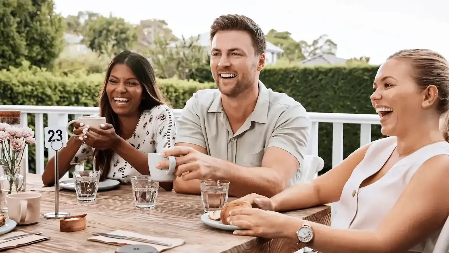 a group of people are sitting at a table laughing and drinking coffee .