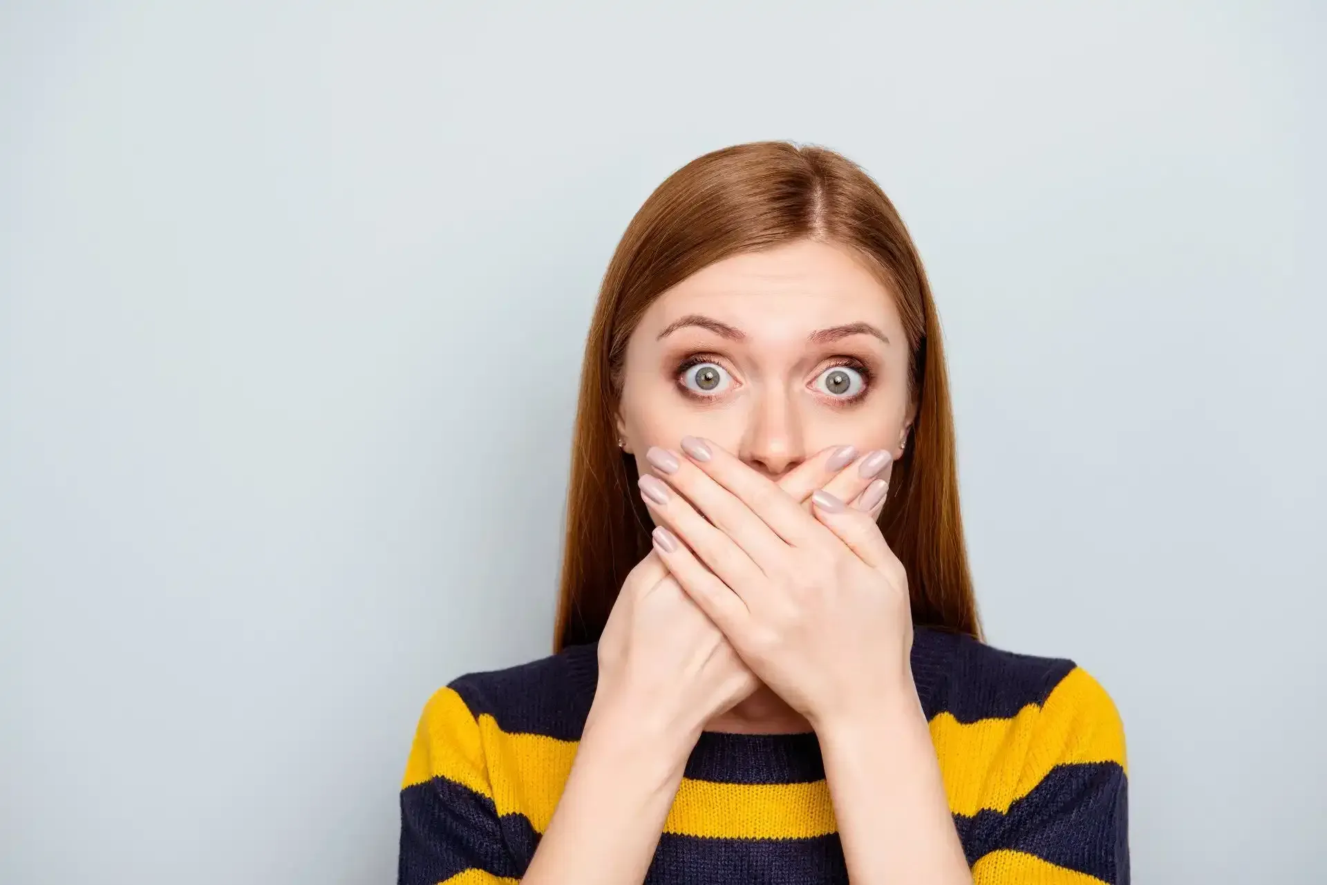 a woman is covering her mouth with her hands .