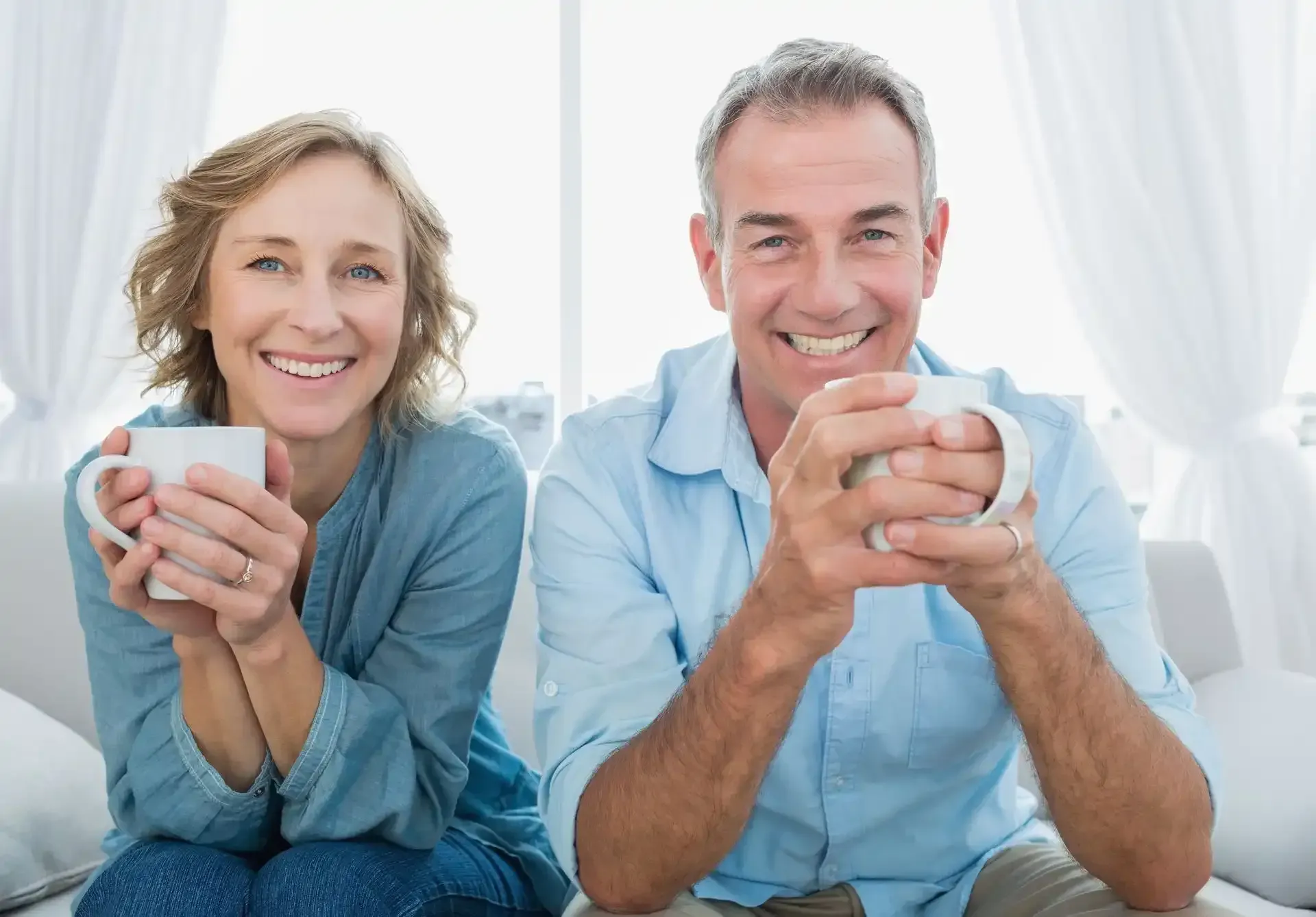 A Man And A Woman Sitting On A Couch Holding Coffee Mugs