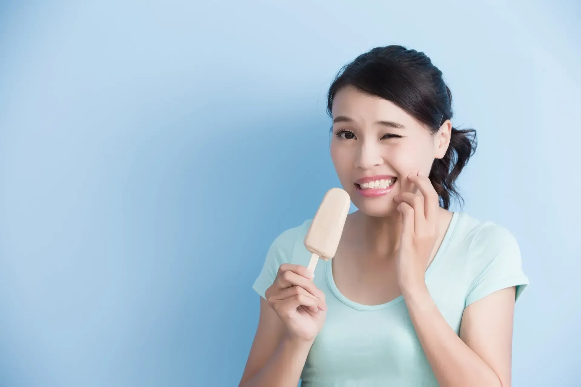 A woman is holding an ice cream bar in her hand and has a toothache.