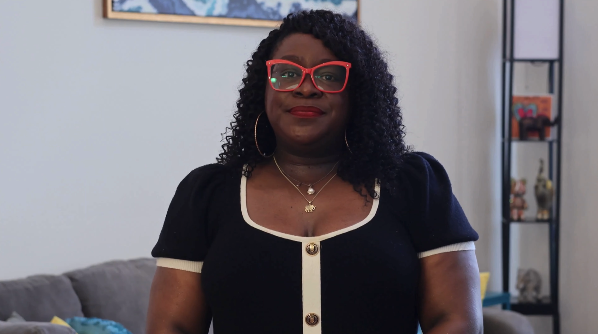 Dr. Ashley standing in a bright room, wearing red glasses and a black dress with white trim.