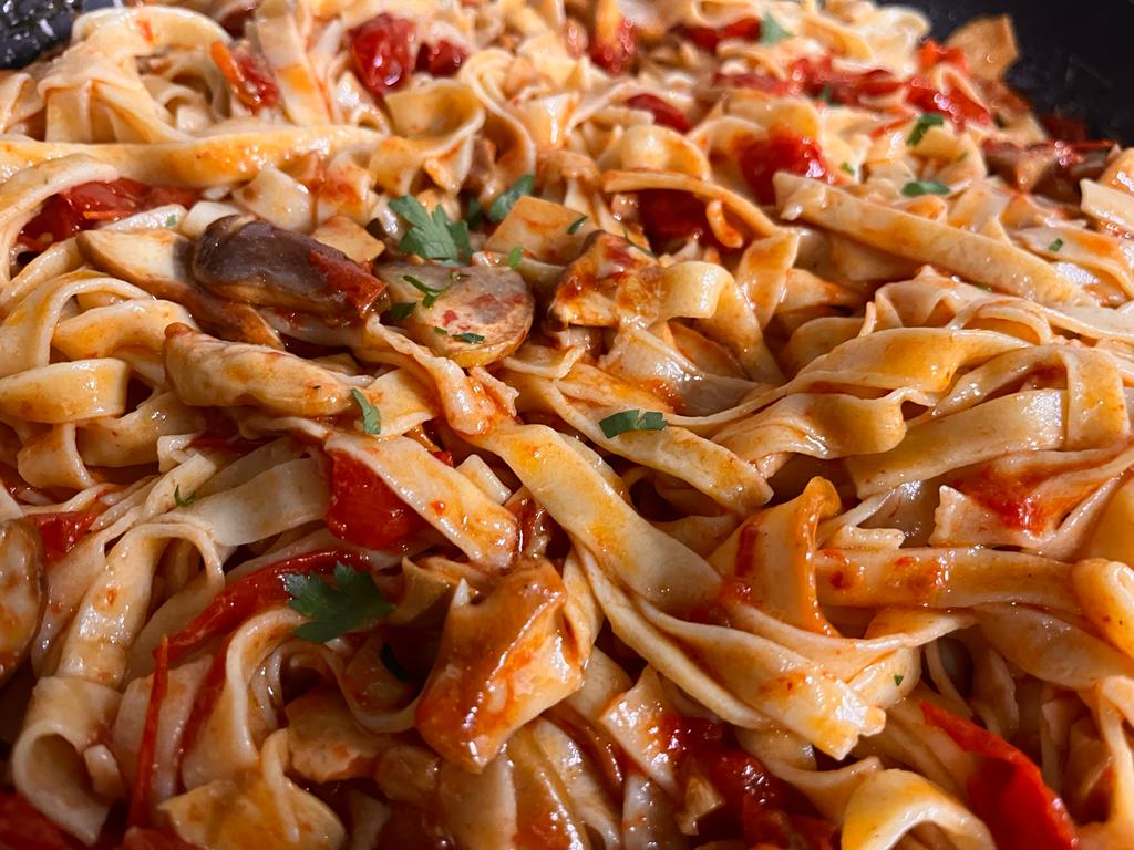Primo piano di fettuccine condite con salsa di pomodoro, funghi a fette ed erbe aromatiche fresche.