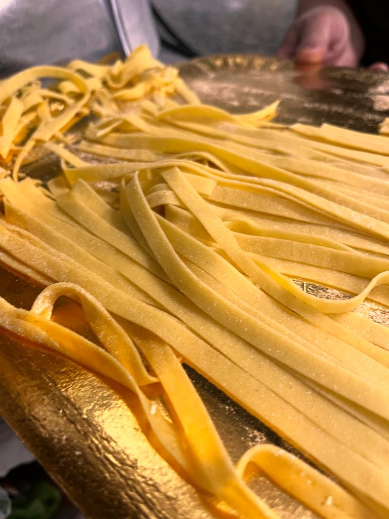 Fettuccine fresche di colore giallo adagiate su una superficie dorata e infarinata.