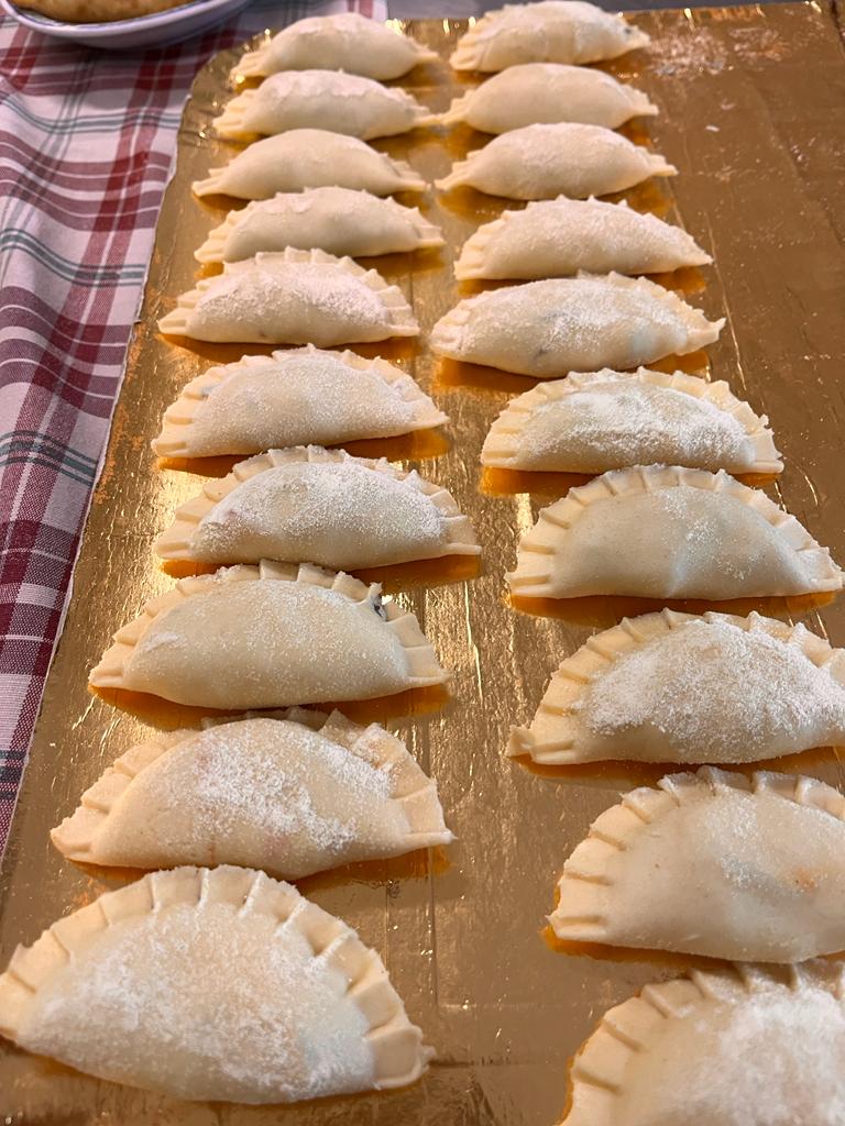 File di gnocchi a forma di mezzaluna, infarinati e disposti su un vassoio color oro.