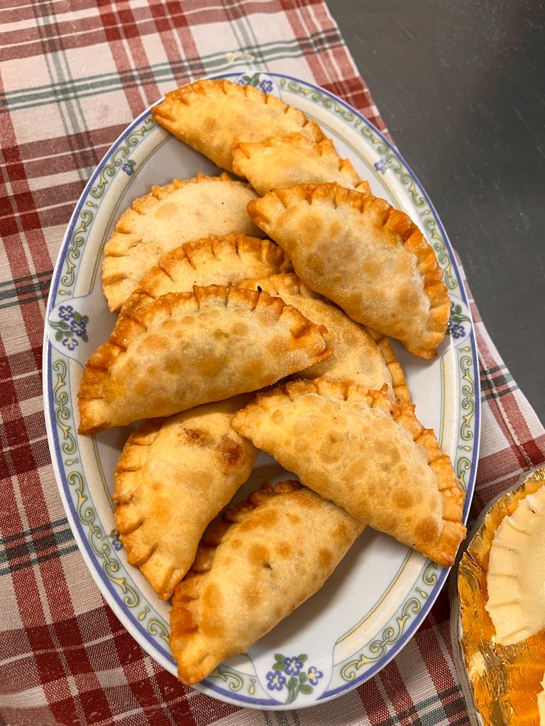 Un piatto di empanadas fritte a forma di mezzaluna, di colore marrone dorato, disposte su una tovaglia a quadri rossi e bianchi.