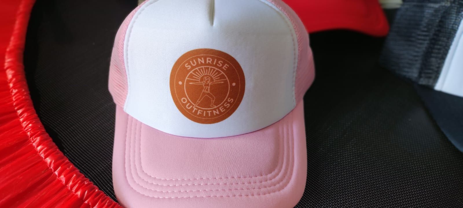 Una gorra de camionero rosa, blanca y marrón con un logotipo que dice 
