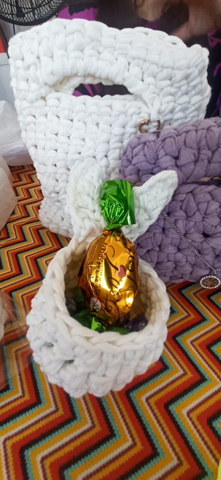 Cesta de Pascua de ganchillo con huevo de chocolate y bolsa blanca sobre fondo estampado.