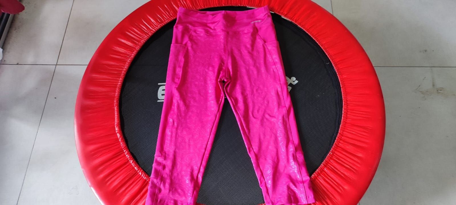 Leggings rosas extendidas sobre una cama elástica negra con borde rojo.